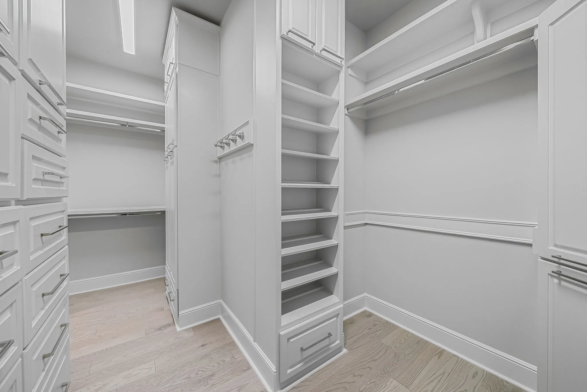 Custom built-in closet system featuring extensive shelving, hanging rods, drawer storage, and light wood-finish flooring