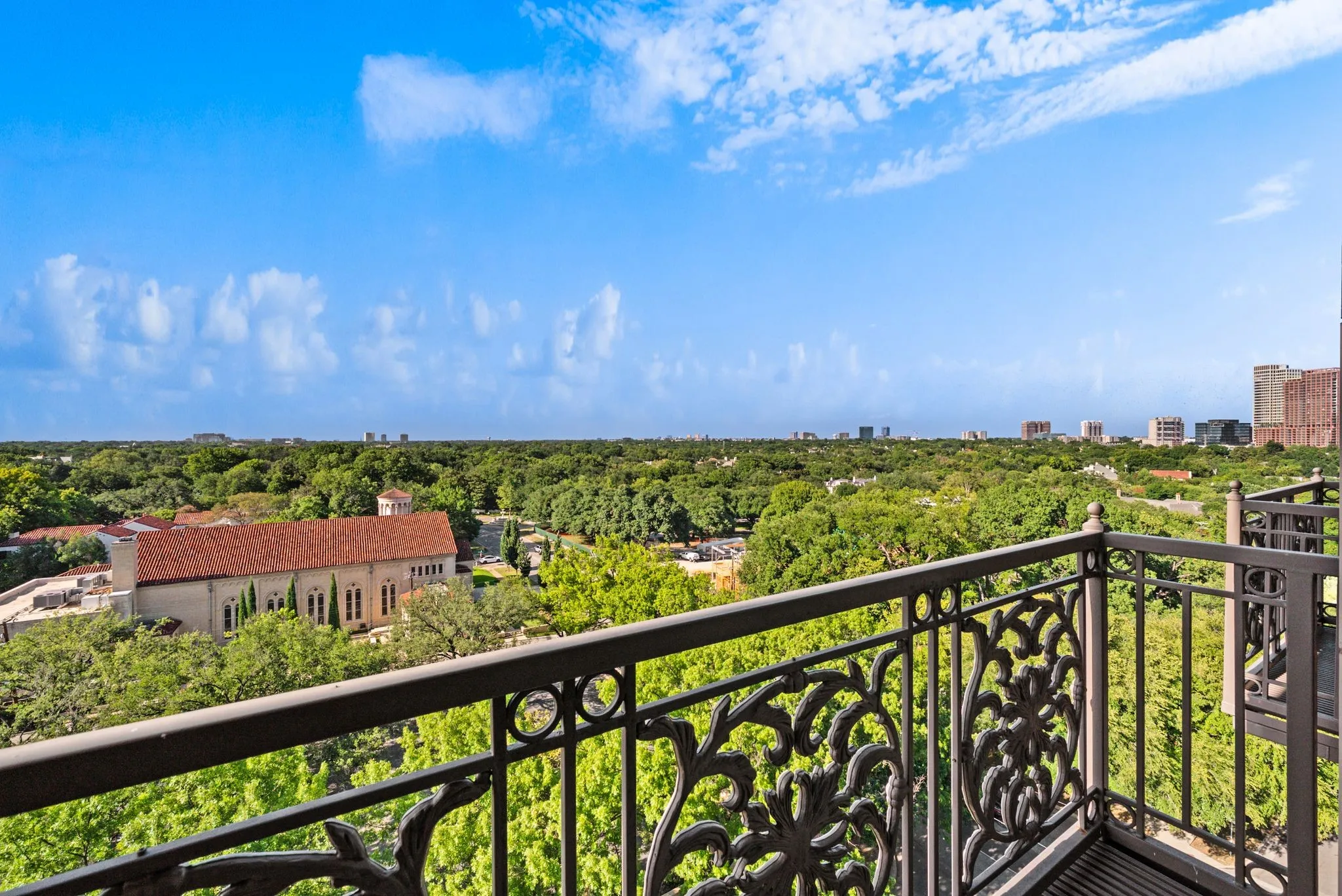 Balcony with ornate wrought iron railing overlooking a tree-lined urban landscape