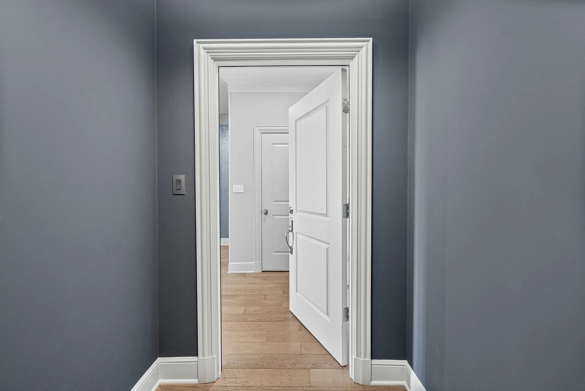 Hallway featuring a neutral wall color, white trim, and wood-finish flooring extending into the adjoining room