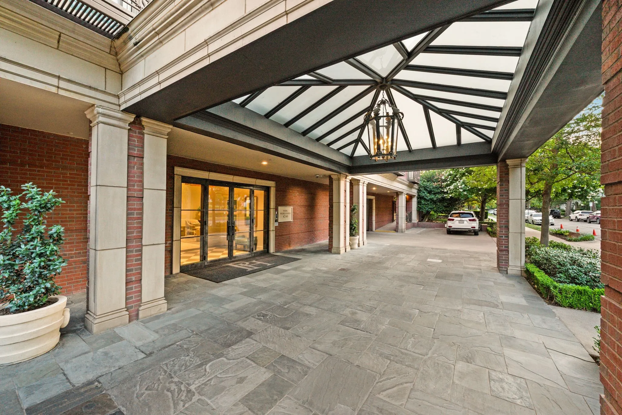 Elegant porte-cochere entrance featuring a glass and metal canopy, stone tile flooring, and a large hanging lantern