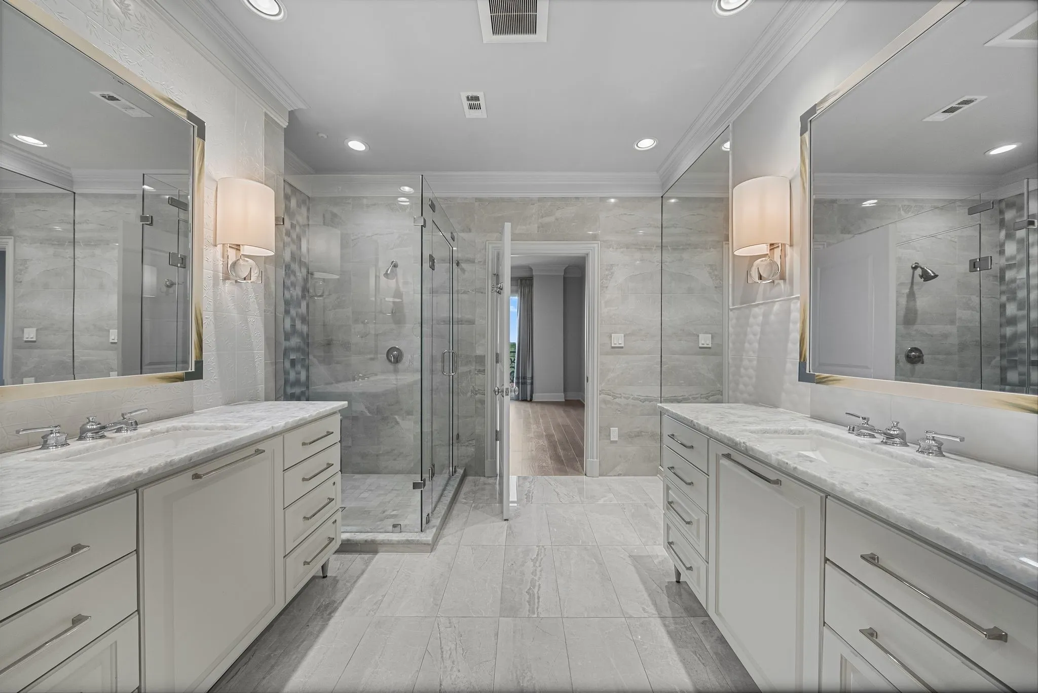 Spacious bathroom featuring dual vanities with integrated sinks, framed mirrors, and wall sconces
