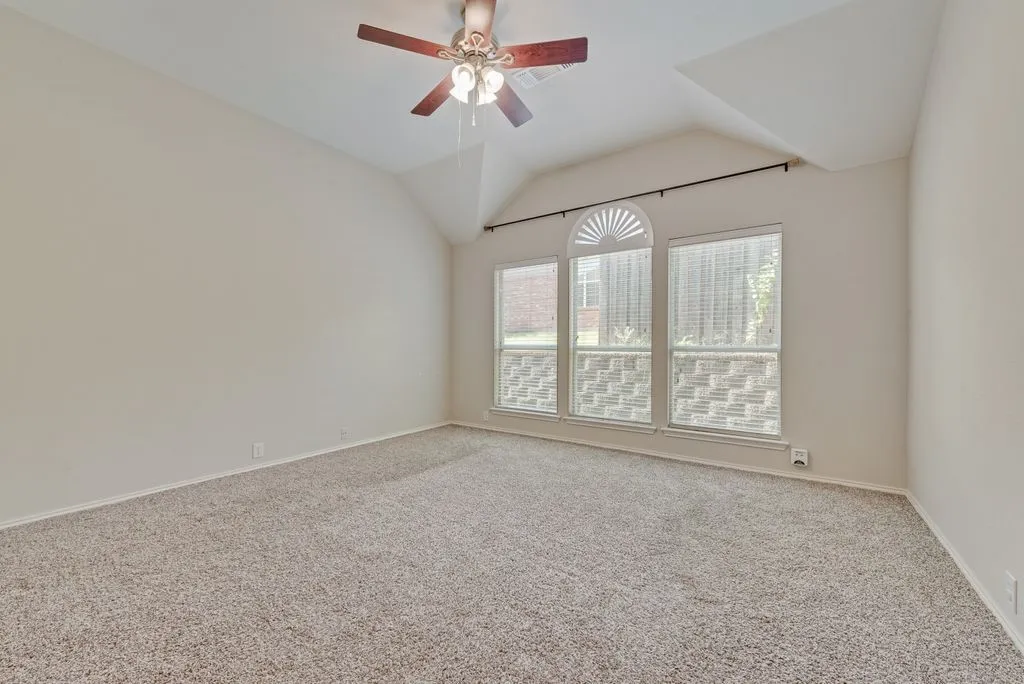 Vaulted ceiling room featuring a decorative arched window with two rectangular windows, beige wall paint, and a ceiling fan with light fixture