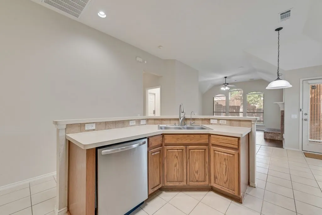Kitchen peninsula featuring light wood-finish cabinetry, a double basin sink, and a stainless steel dishwasher