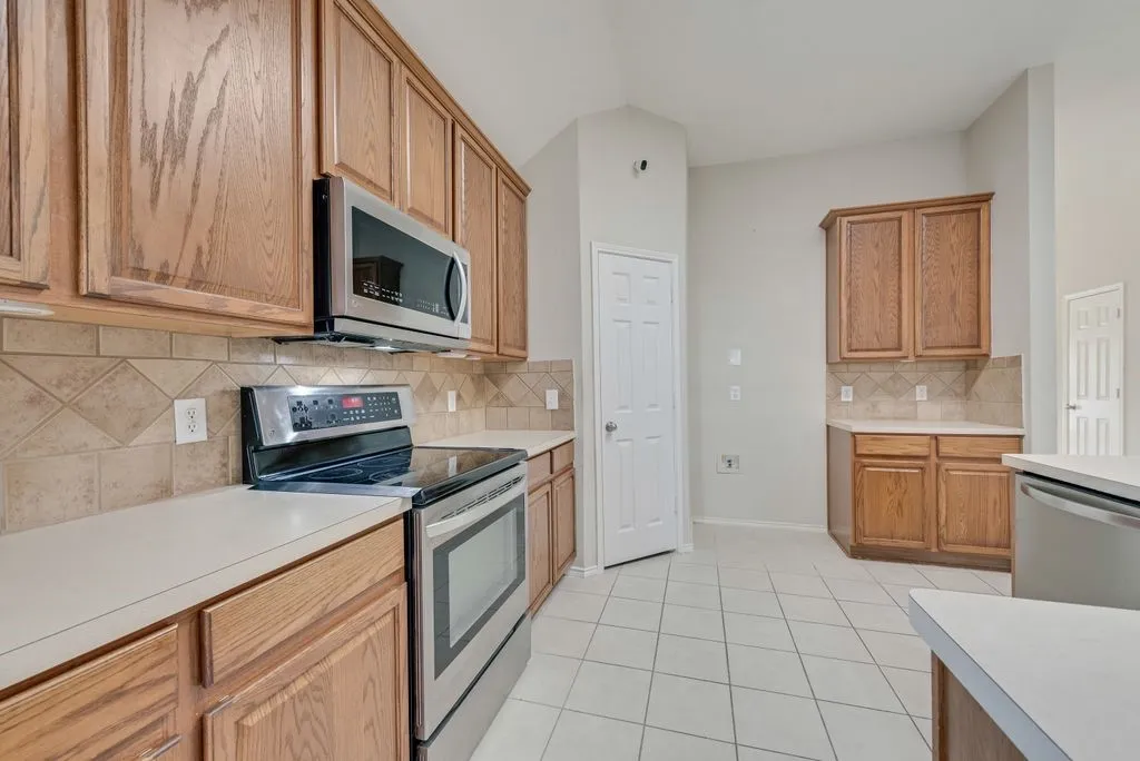 Kitchen featuring wood cabinetry, stainless steel appliances, light countertops, and a tiled backsplash
