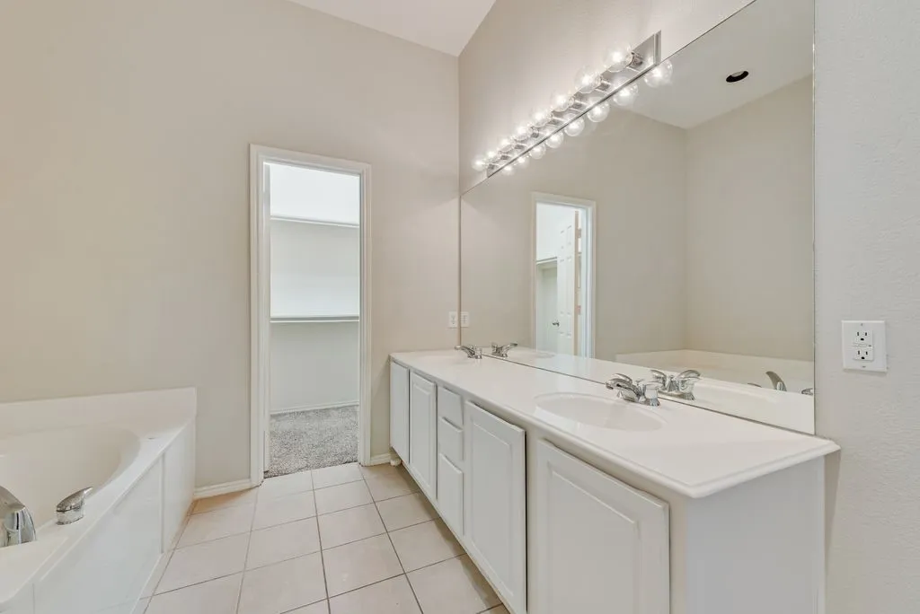 Bathroom featuring a dual vanity with undermount sinks, a wide mirror, and a built-in garden tub