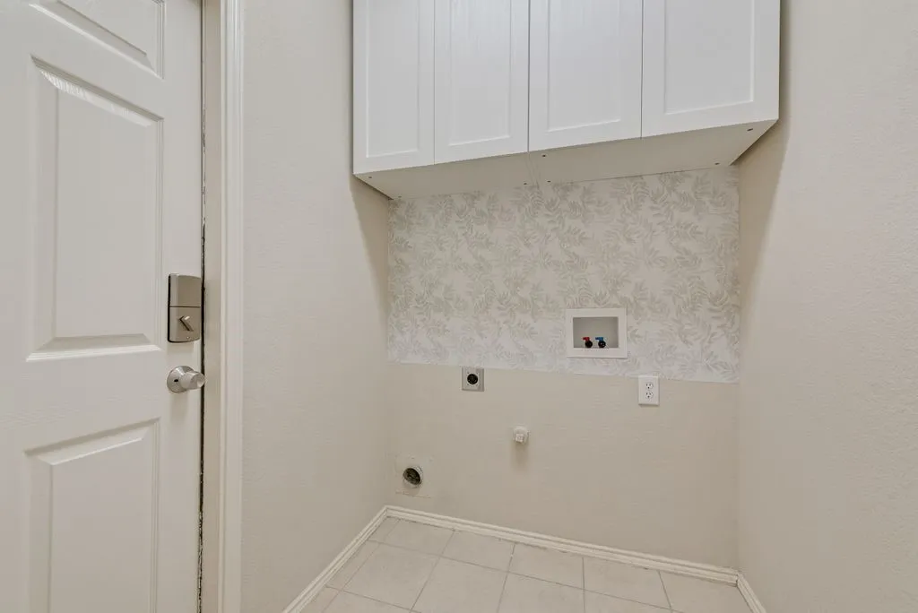 Laundry area featuring white shaker-style cabinetry, a decorative accent wall, and tiled flooring