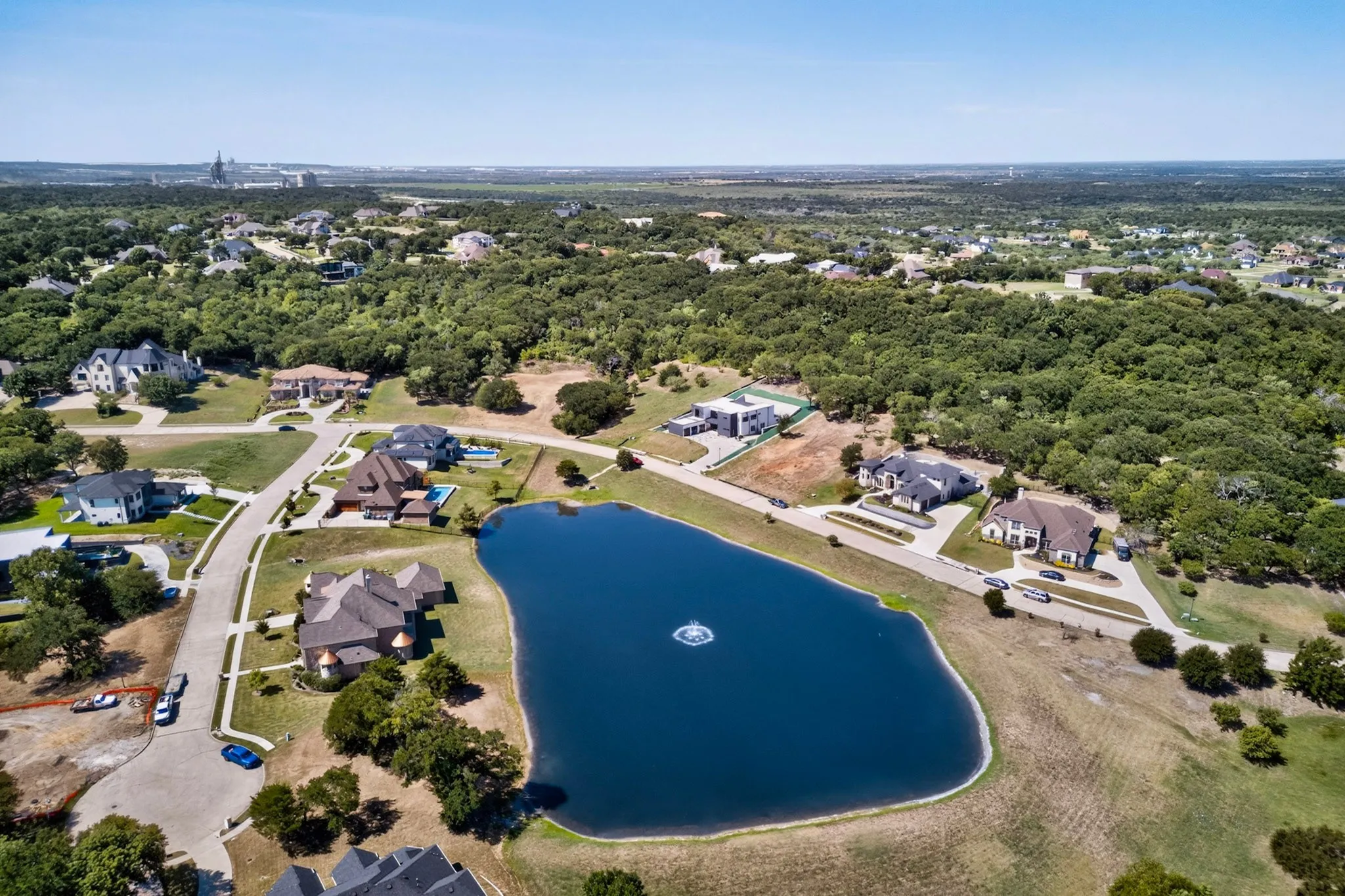 Expansive residential development featuring a central pond with fountain, mature trees, paved streets, and numerous properties with private pools