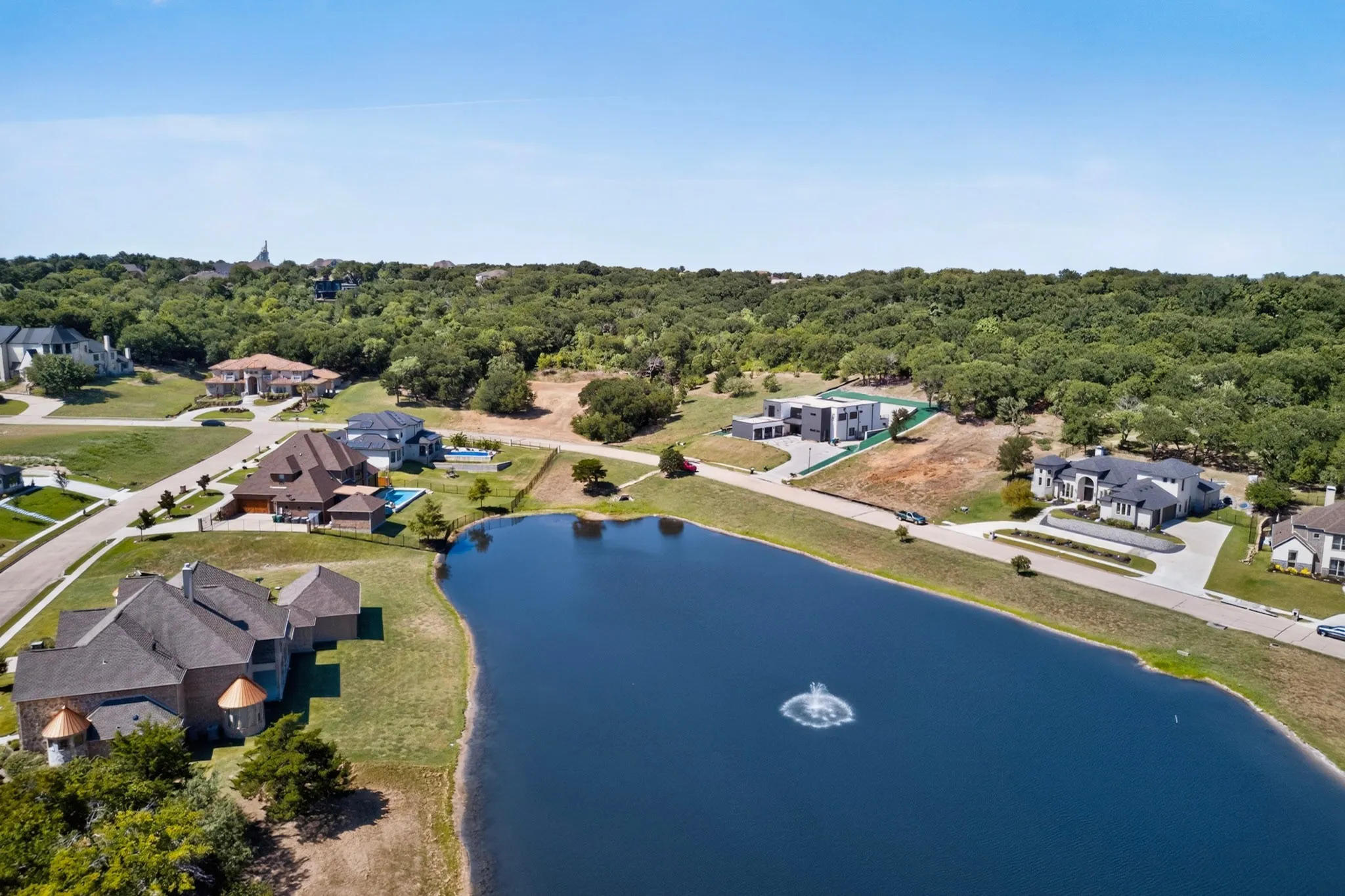 Expansive lake with fountain feature, bordered by substantial properties and mature tree lines