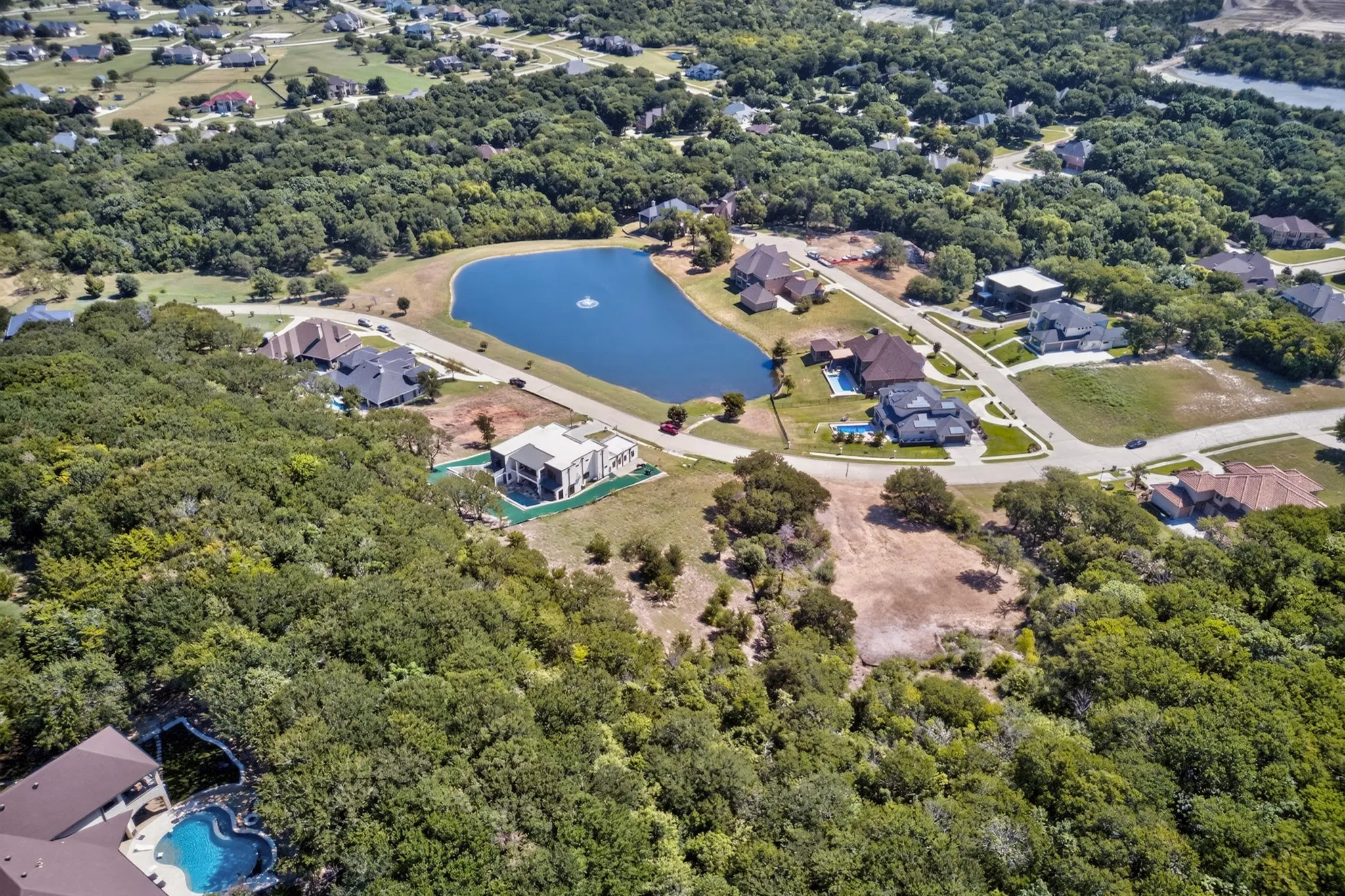 Lush, tree-filled landscape surrounds a residential area with a prominent pond featuring a central water fountain