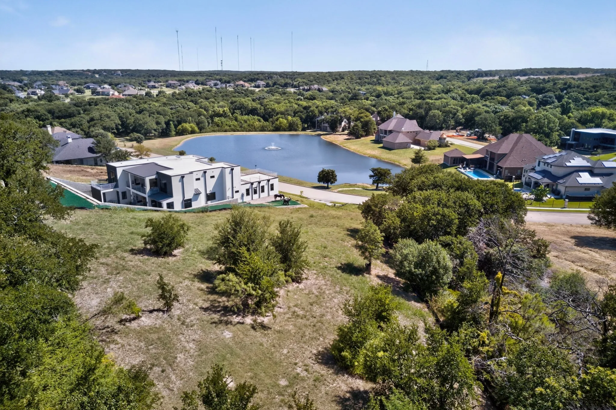 Expansive residential landscape featuring a central lake with a fountain, surrounded by mature trees and varied architectural styles