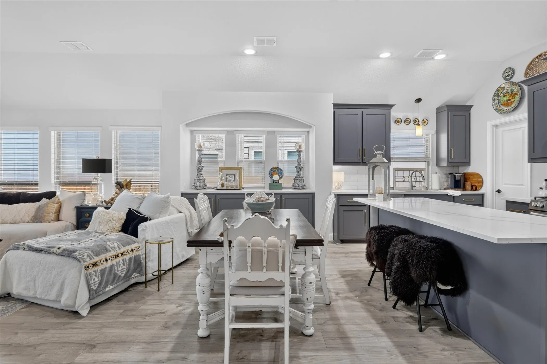 Open-concept living space featuring wood-finish flooring, recessed lighting, and a kitchen with gray cabinetry and white subway tile backsplash