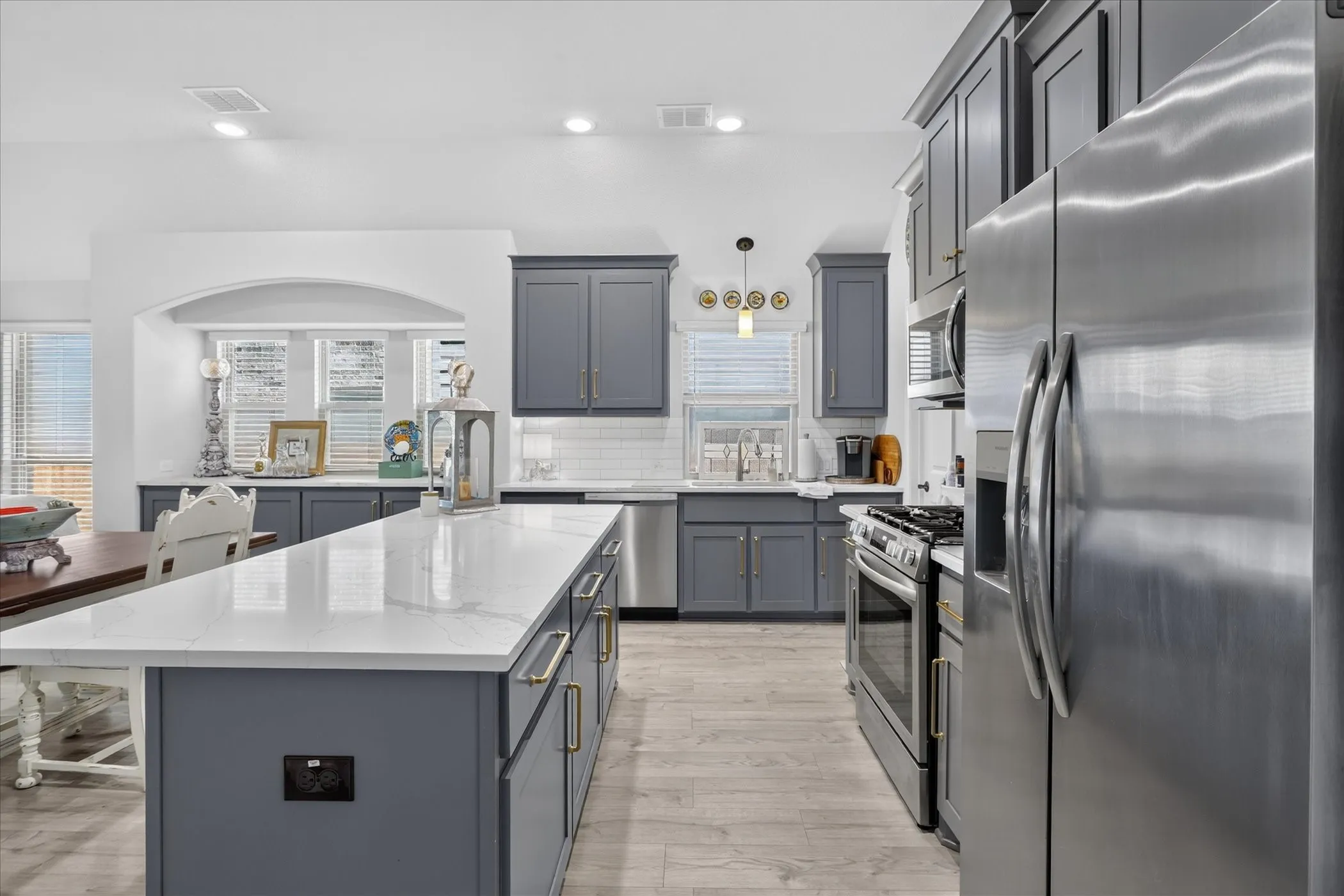 Kitchen featuring a large center island with a white countertop and dark gray cabinetry, stainless steel appliances, white subway tile backsplash, and wood-finish flooring