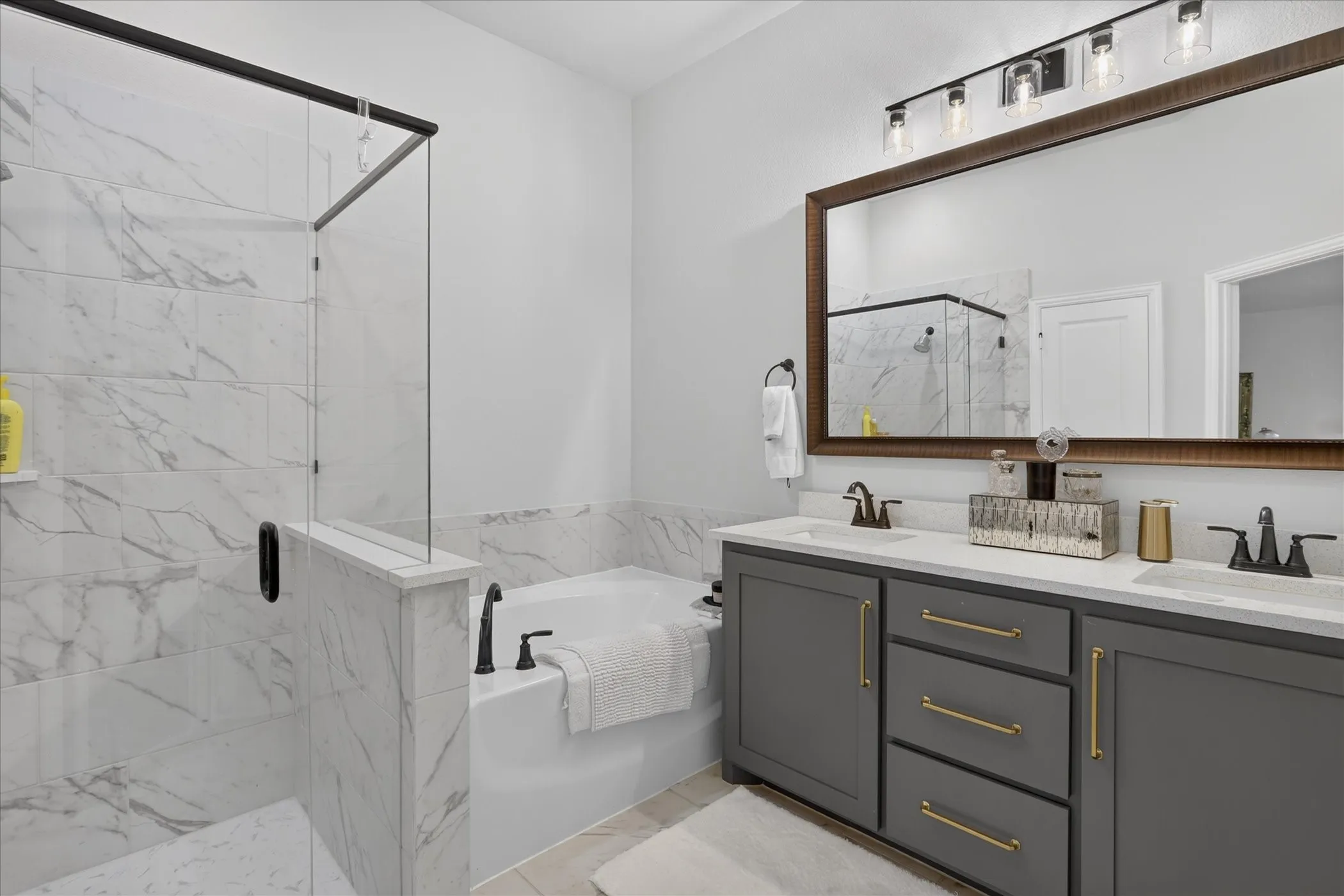 Bathroom featuring a glass-enclosed shower with marble-look tile, a separate built-in soaking tub, and a dual vanity with a white countertop and dark gray cabinetry