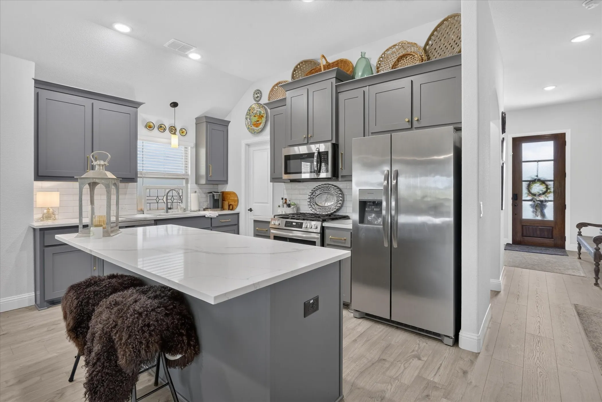 Kitchen featuring a central island with a light-colored countertop, gray cabinetry, stainless steel appliances, and a subway tile backsplash