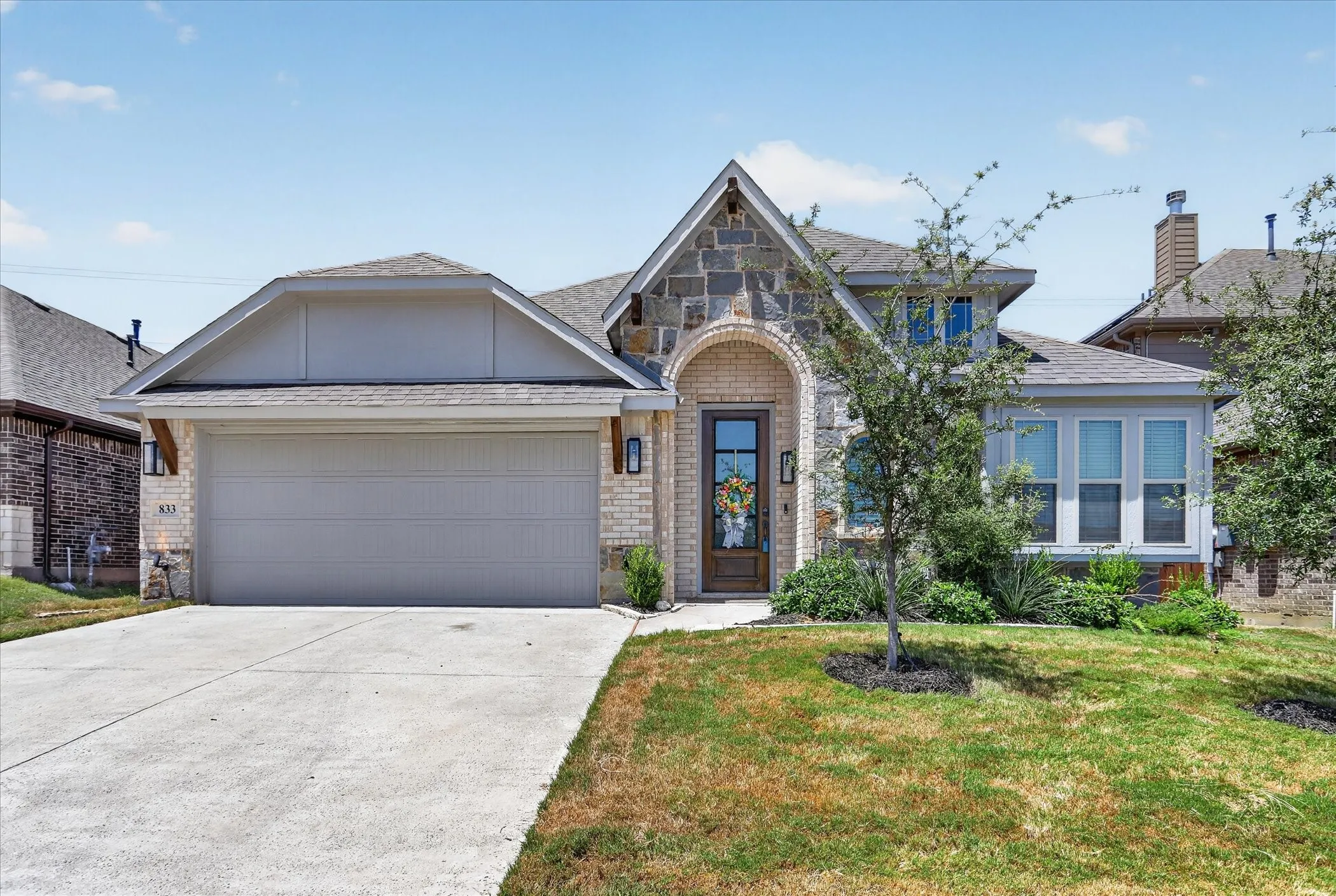 Stone and brick facade home featuring an arched entryway, transom window above the front door, and a two-car garage