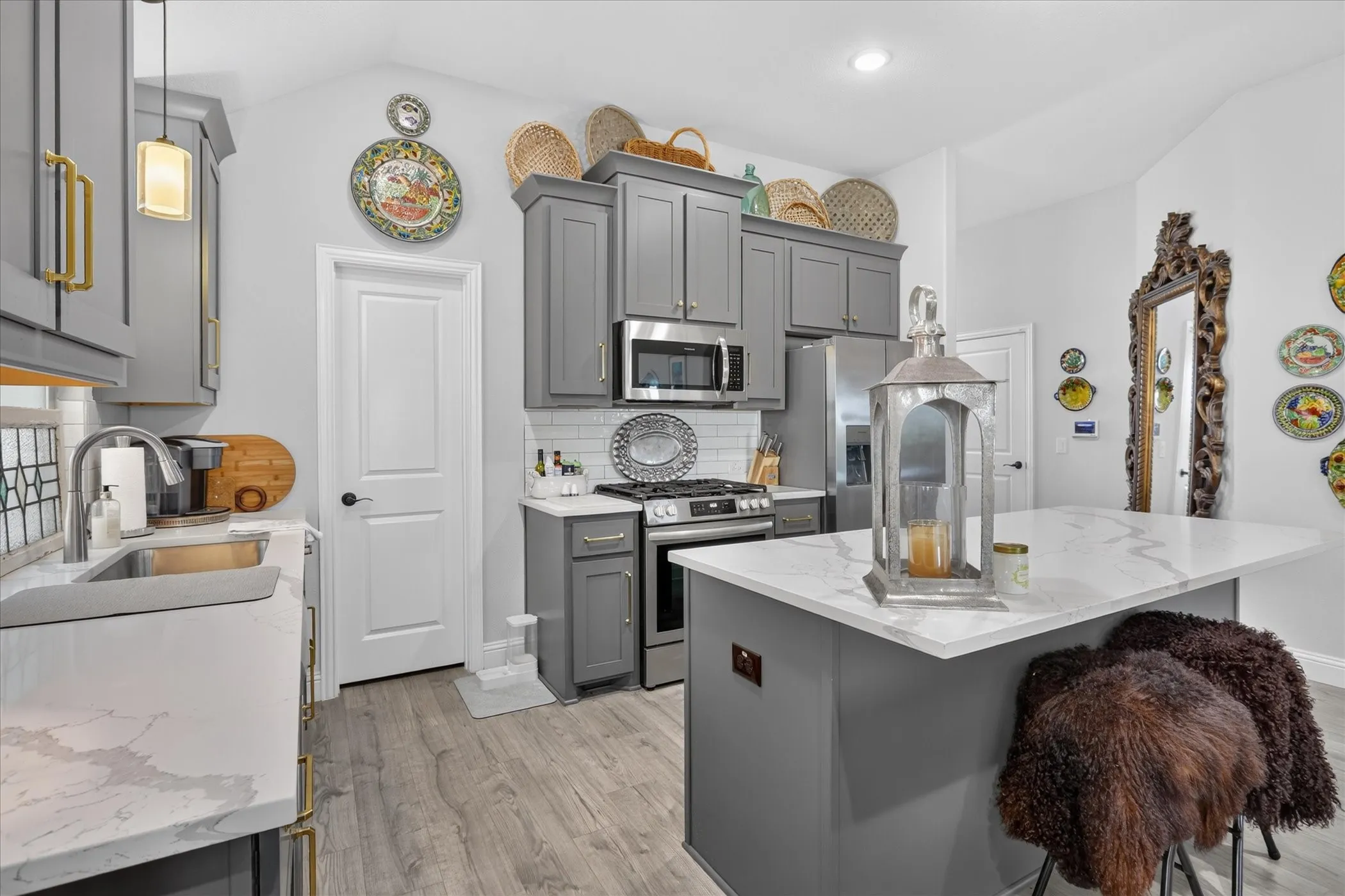Kitchen featuring grey cabinetry with gold-toned hardware, stainless steel appliances, a white subway tile backsplash, and wood-finish flooring