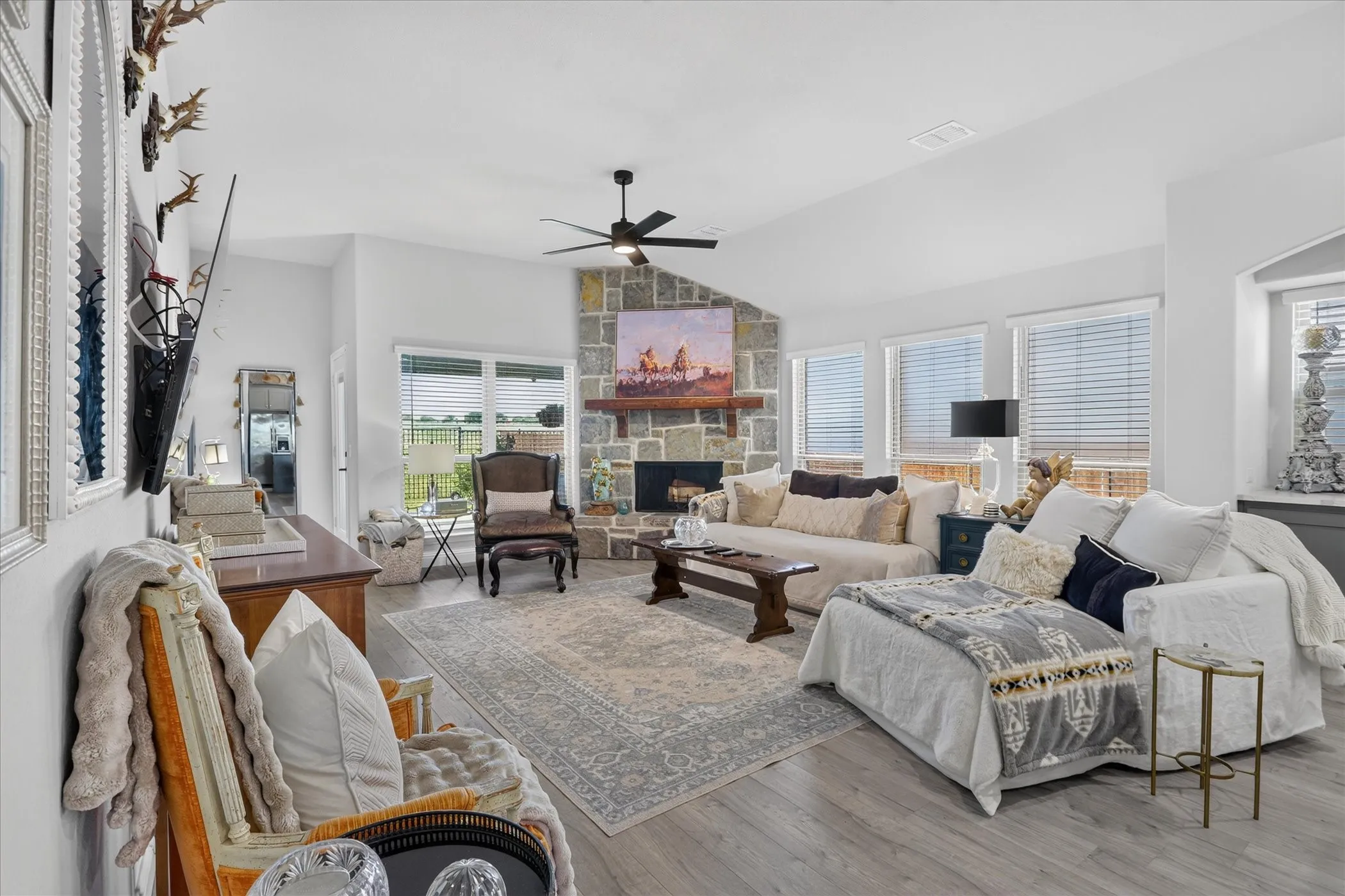 Spacious living area featuring a stone fireplace with a wood mantel, vaulted ceiling, and wood-finish flooring
