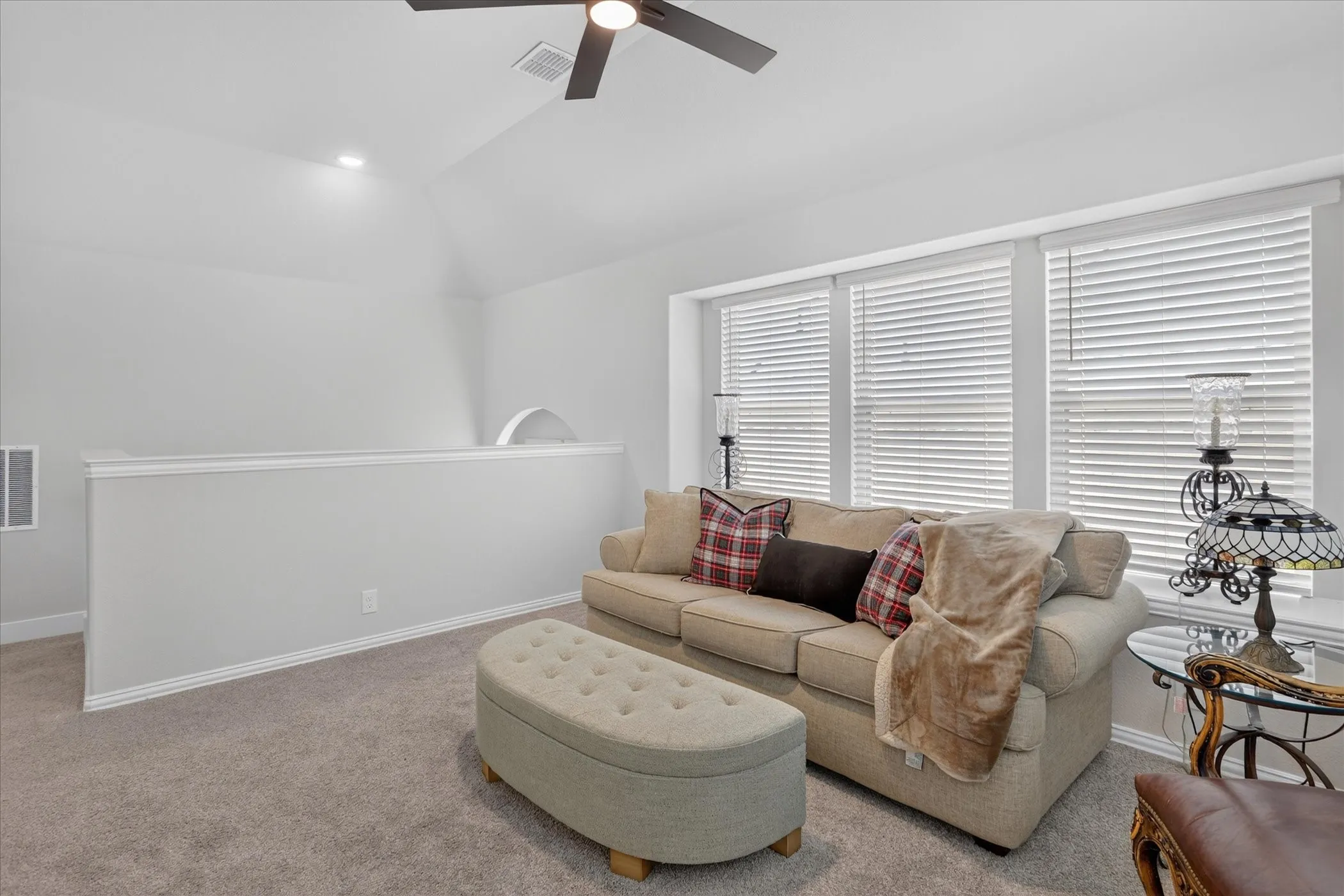 Carpeted secondary living space featuring a vaulted ceiling with a flush-mount ceiling fan, recessed lighting, and multiple windows with horizontal blinds