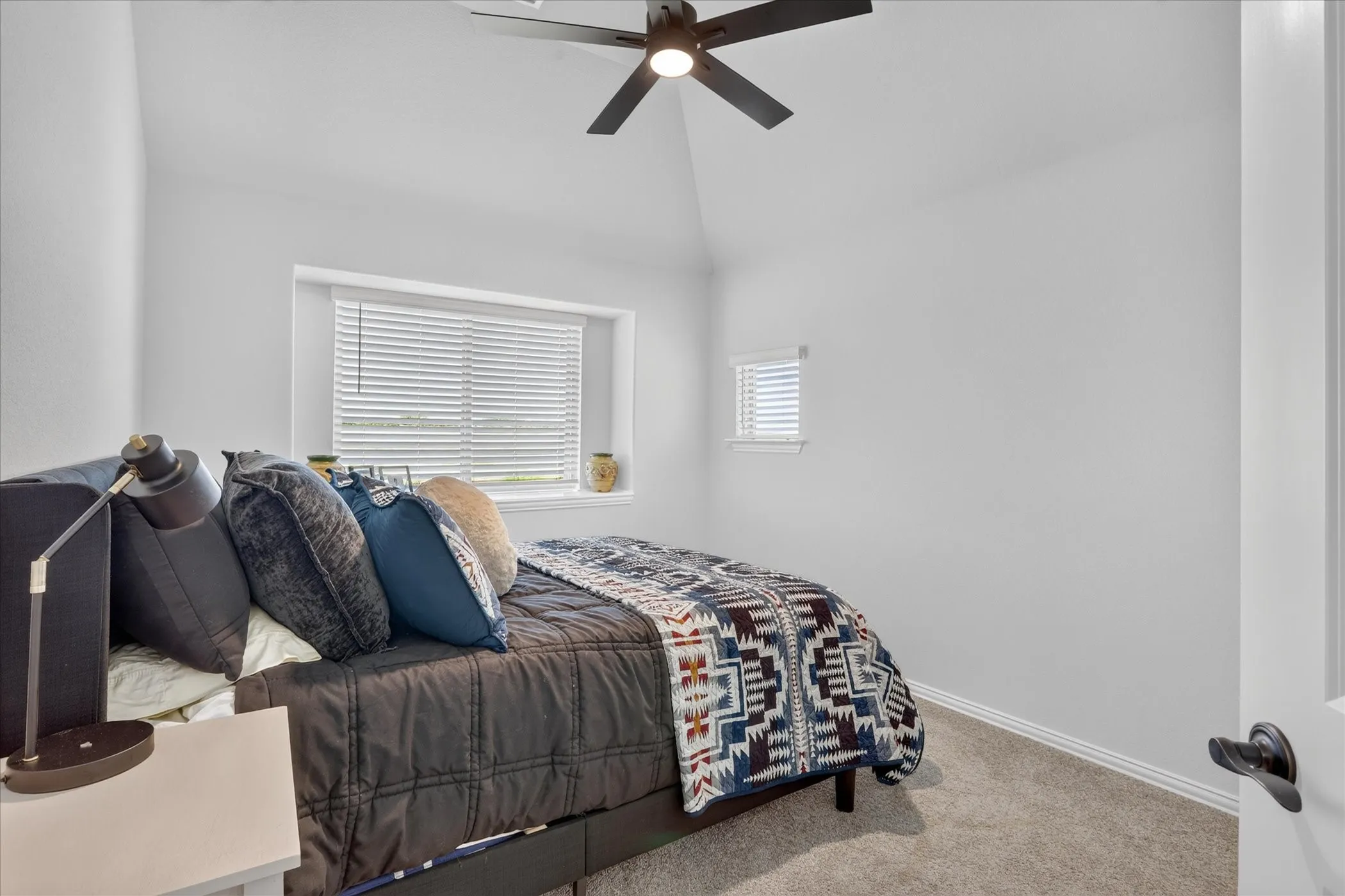 Carpeted room featuring a ceiling fan, vaulted ceiling, and two windows with blinds