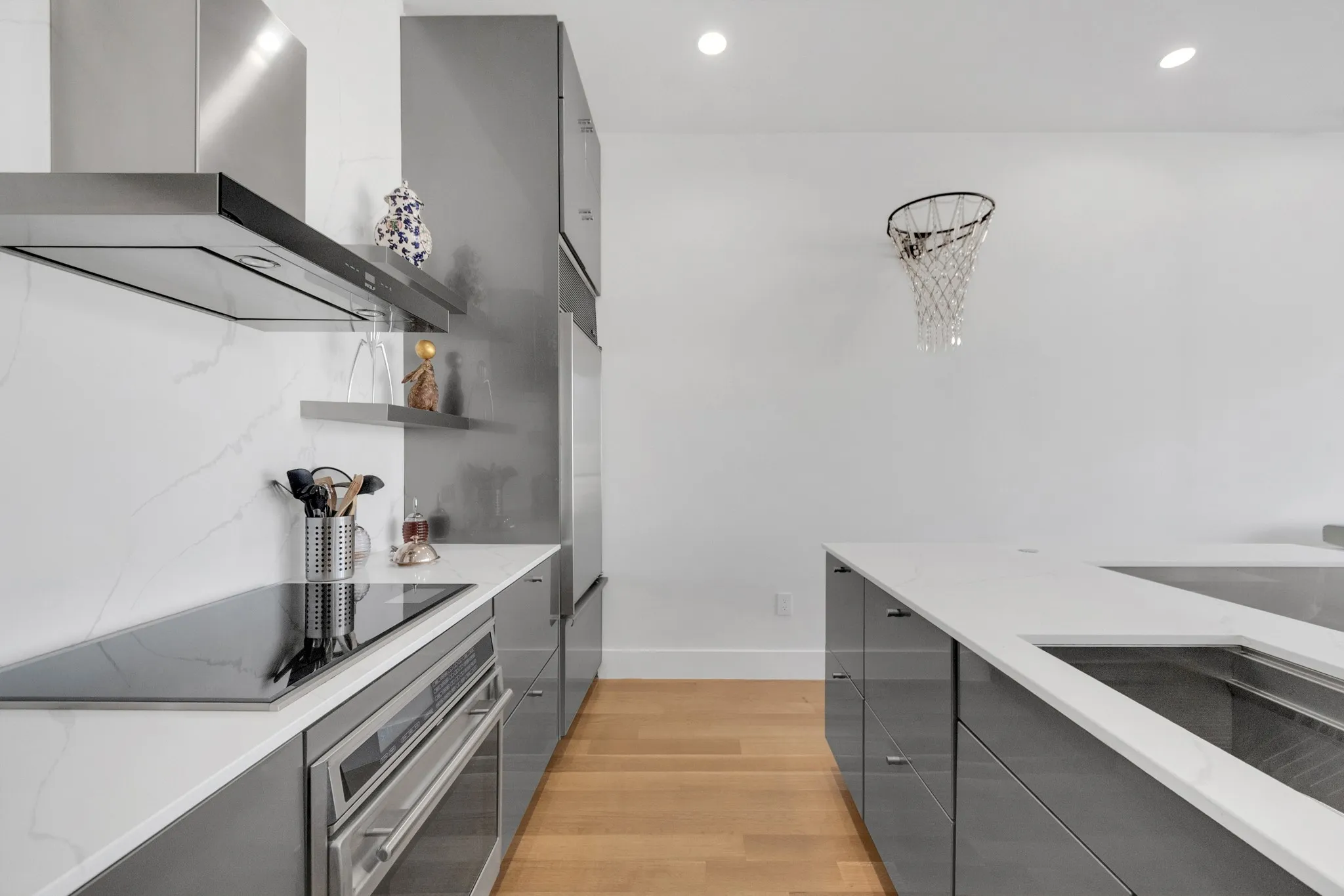 Sleek kitchen featuring gray cabinetry, integrated stainless steel appliances, a built-in cooktop, and a matching range hood