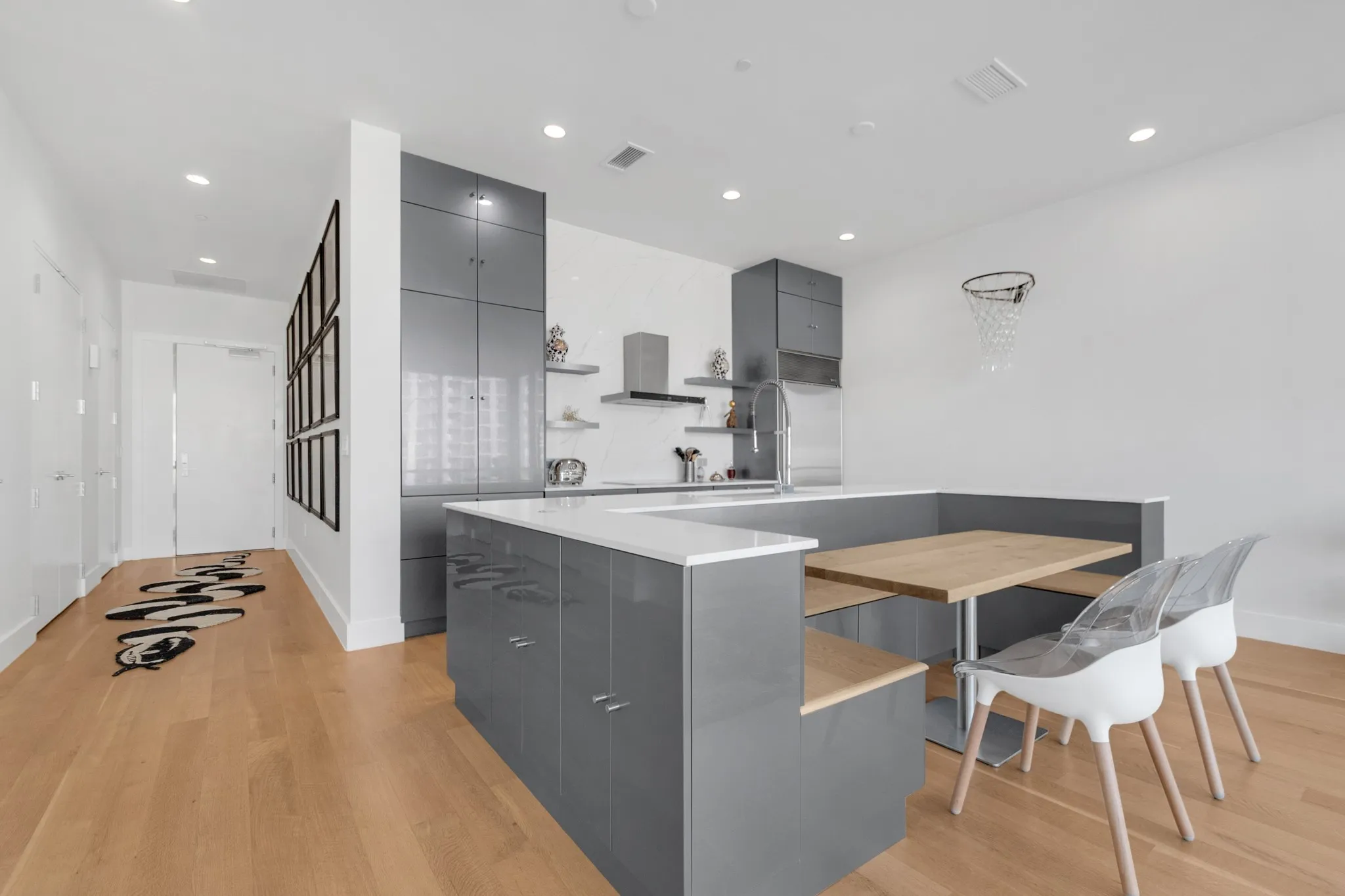 Light wood-finish flooring, recessed lighting, white walls, and a kitchen featuring gray cabinetry with integrated appliances