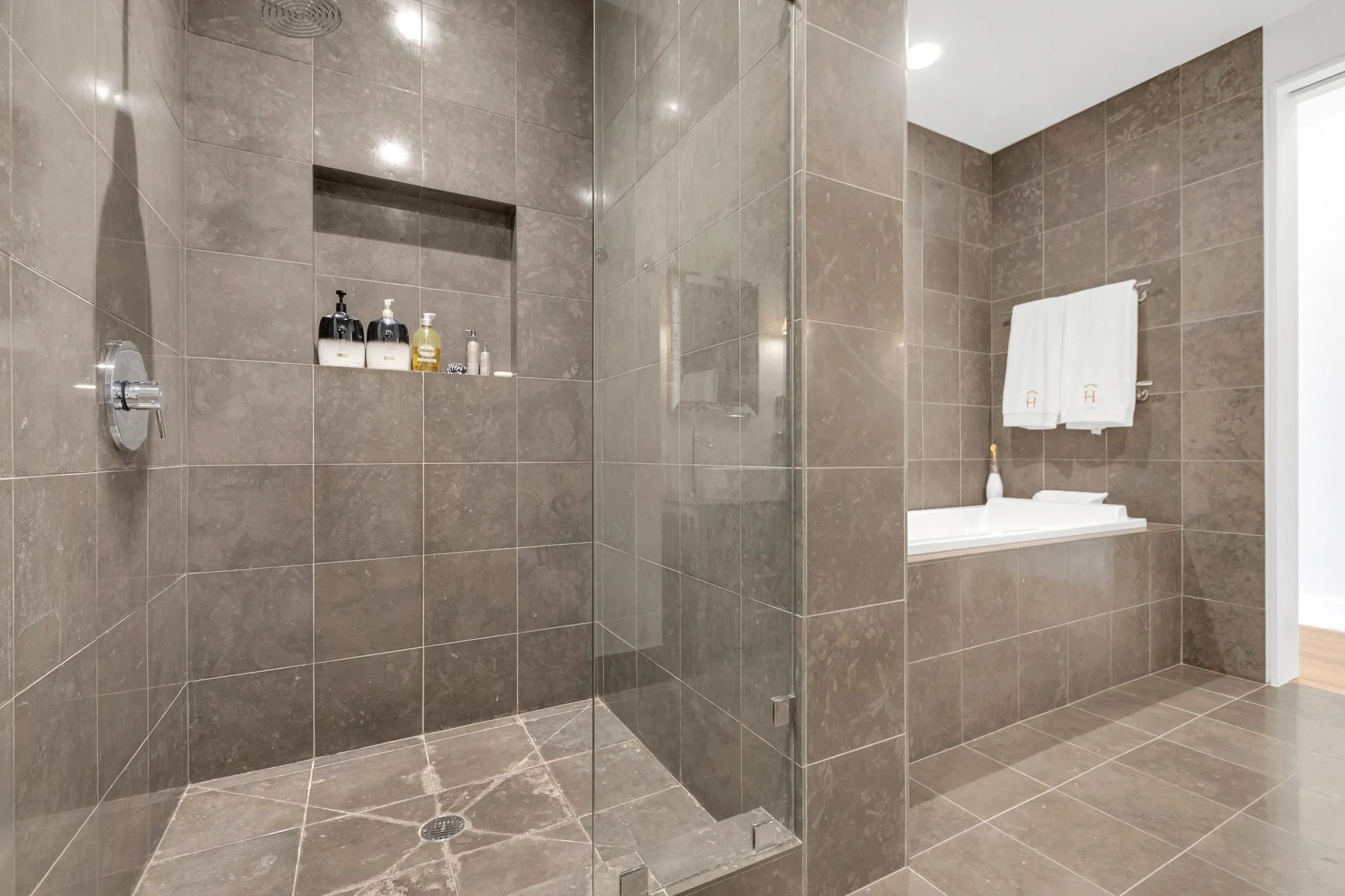 Walk-in shower with glass enclosure, built-in recessed shelf, overhead shower fixture, and tiled floor