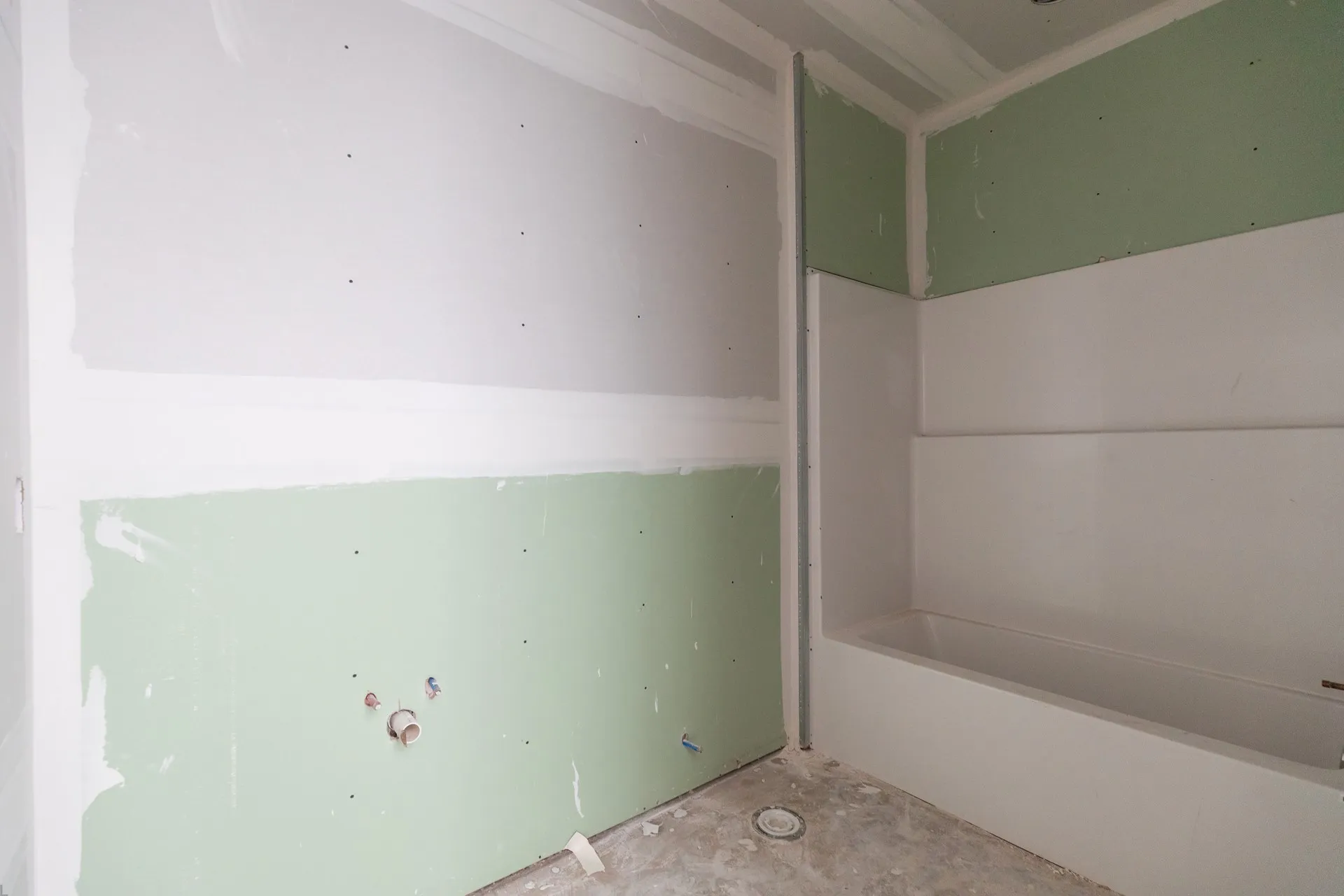 Bathroom under construction featuring a built-in bathtub, green board drywall, and unfinished concrete flooring