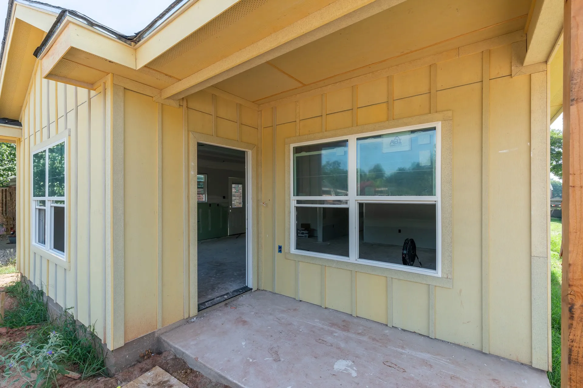 Exterior featuring vertical plank siding, a covered concrete patio, and white-framed windows