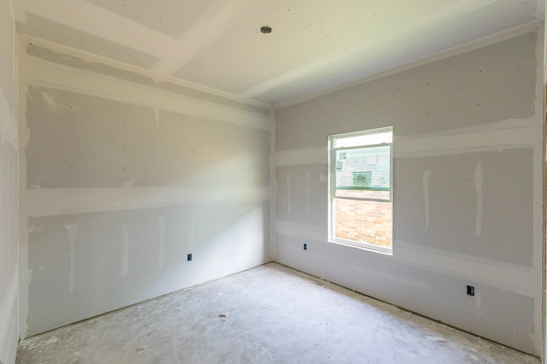 Room in construction phase featuring a window, unpainted drywall, and a ceiling with crown molding