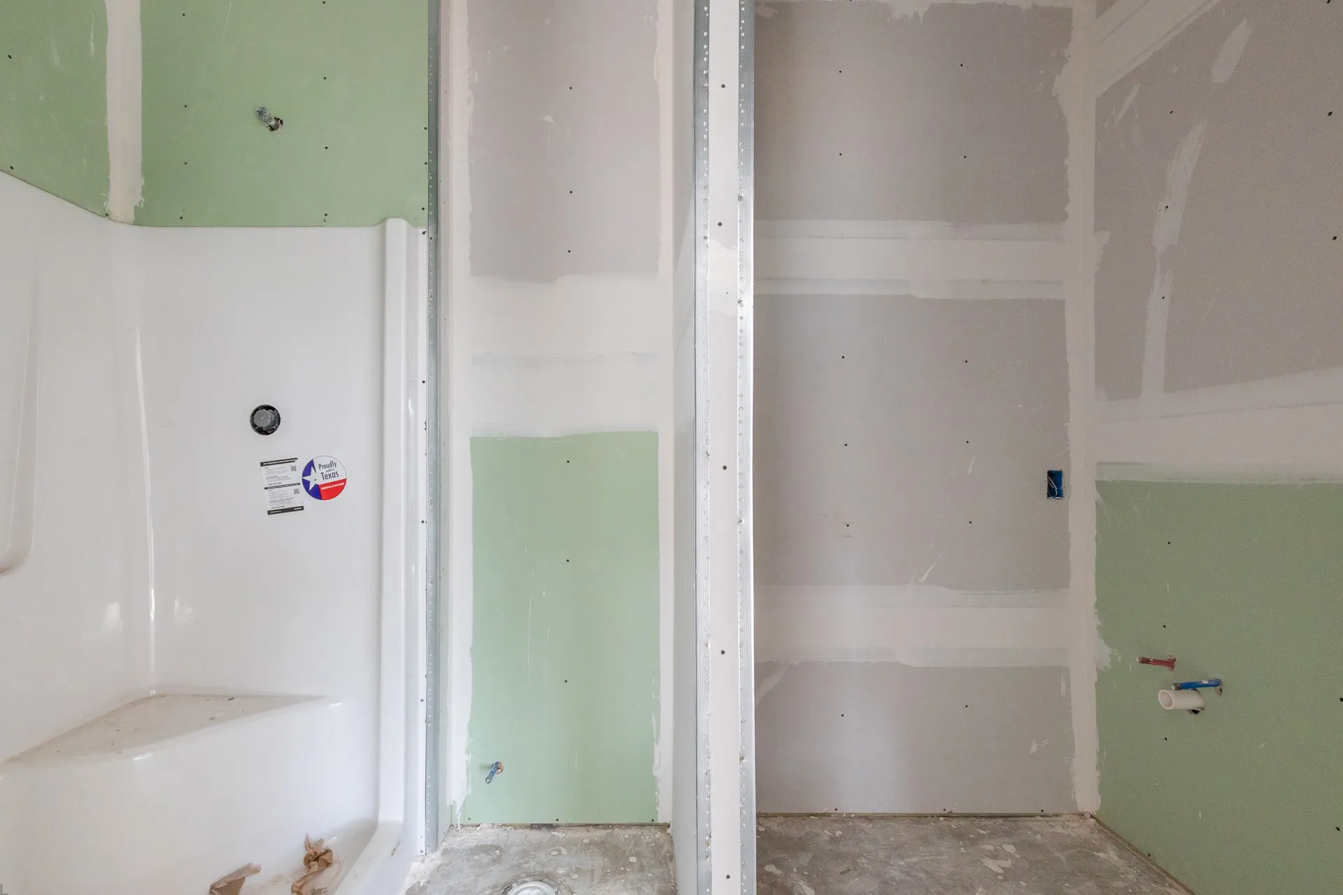 Bathroom under construction with a corner shower base and unfinished drywall