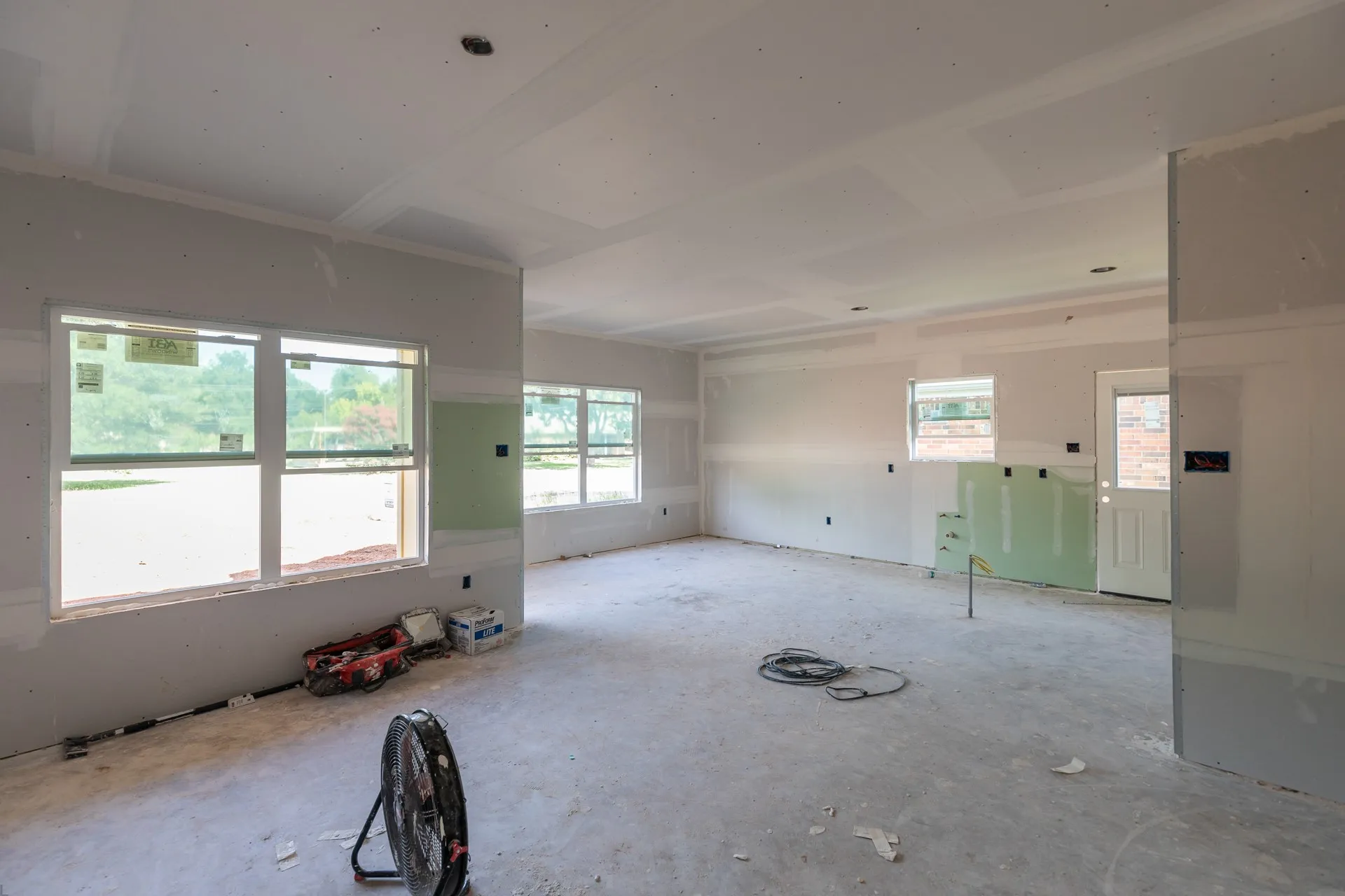 Interior space currently under construction, featuring drywall installation and multiple window openings