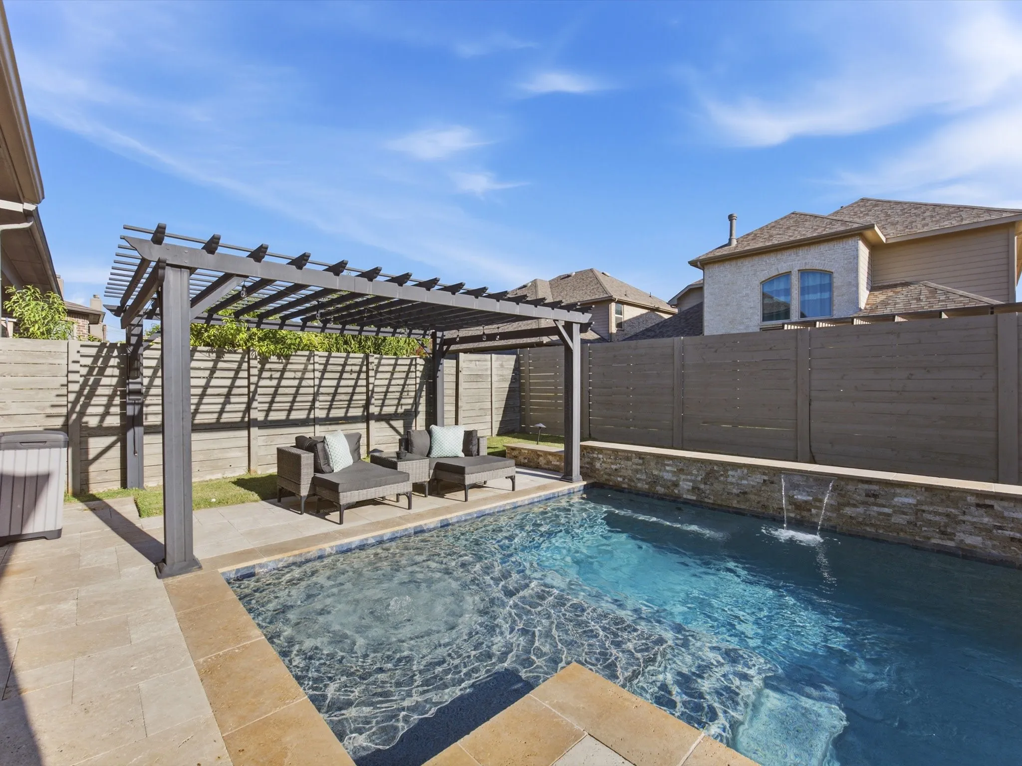 Backyard oasis featuring a rectangular swimming pool with integrated water features and a stone-clad raised wall
