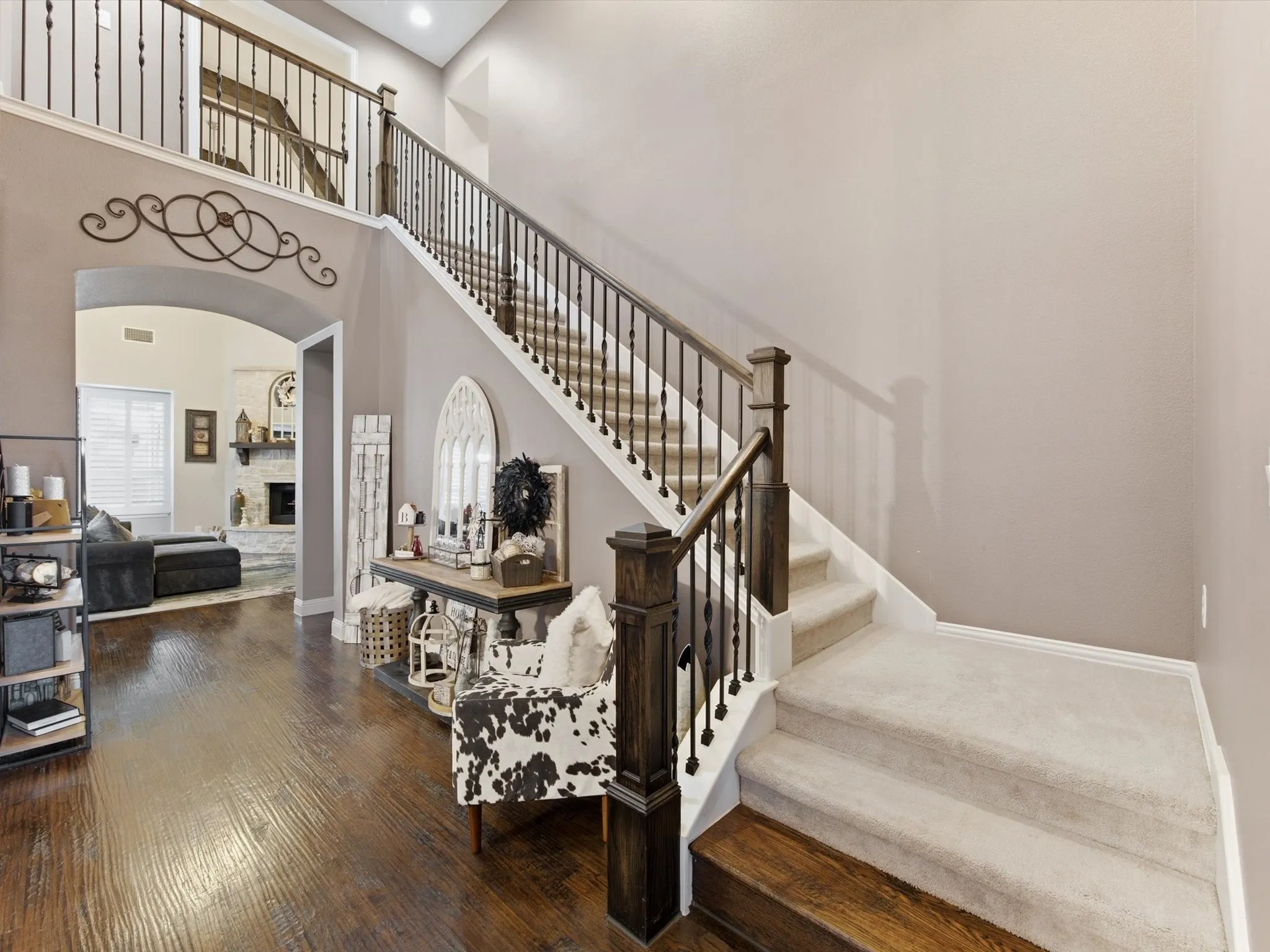 Two-story foyer featuring wood-finish flooring, a carpeted staircase with dark wood banister and wrought iron spindles, and a second-story landing with matching railing