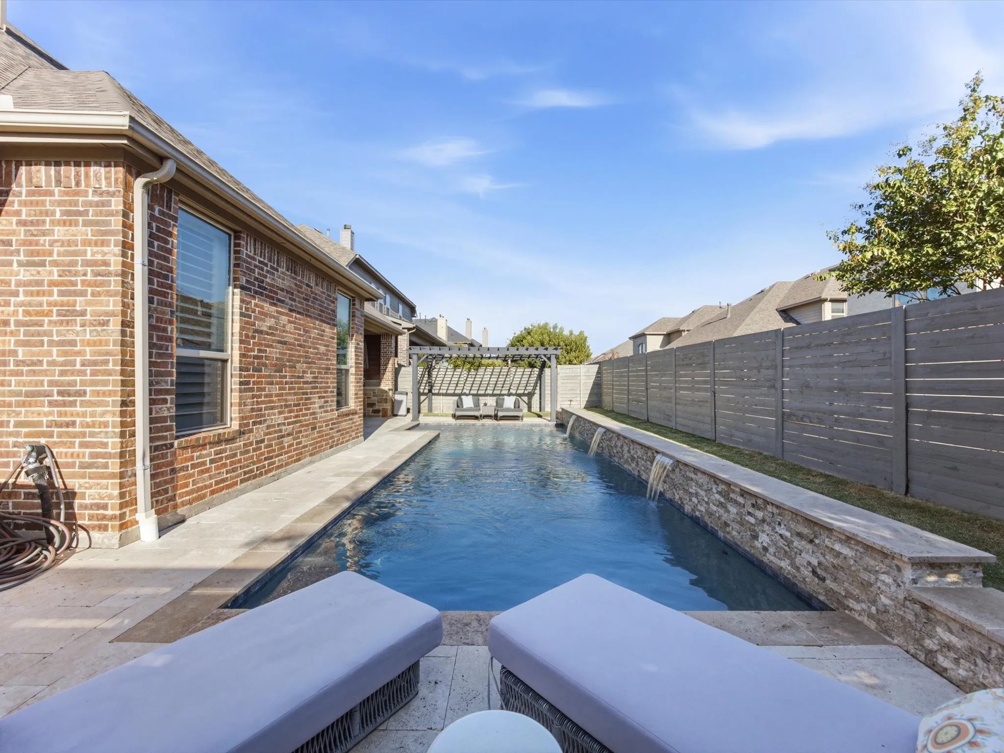 Outdoor swimming pool featuring a stone surround with multiple water features, travertine coping, and a wooden pergola