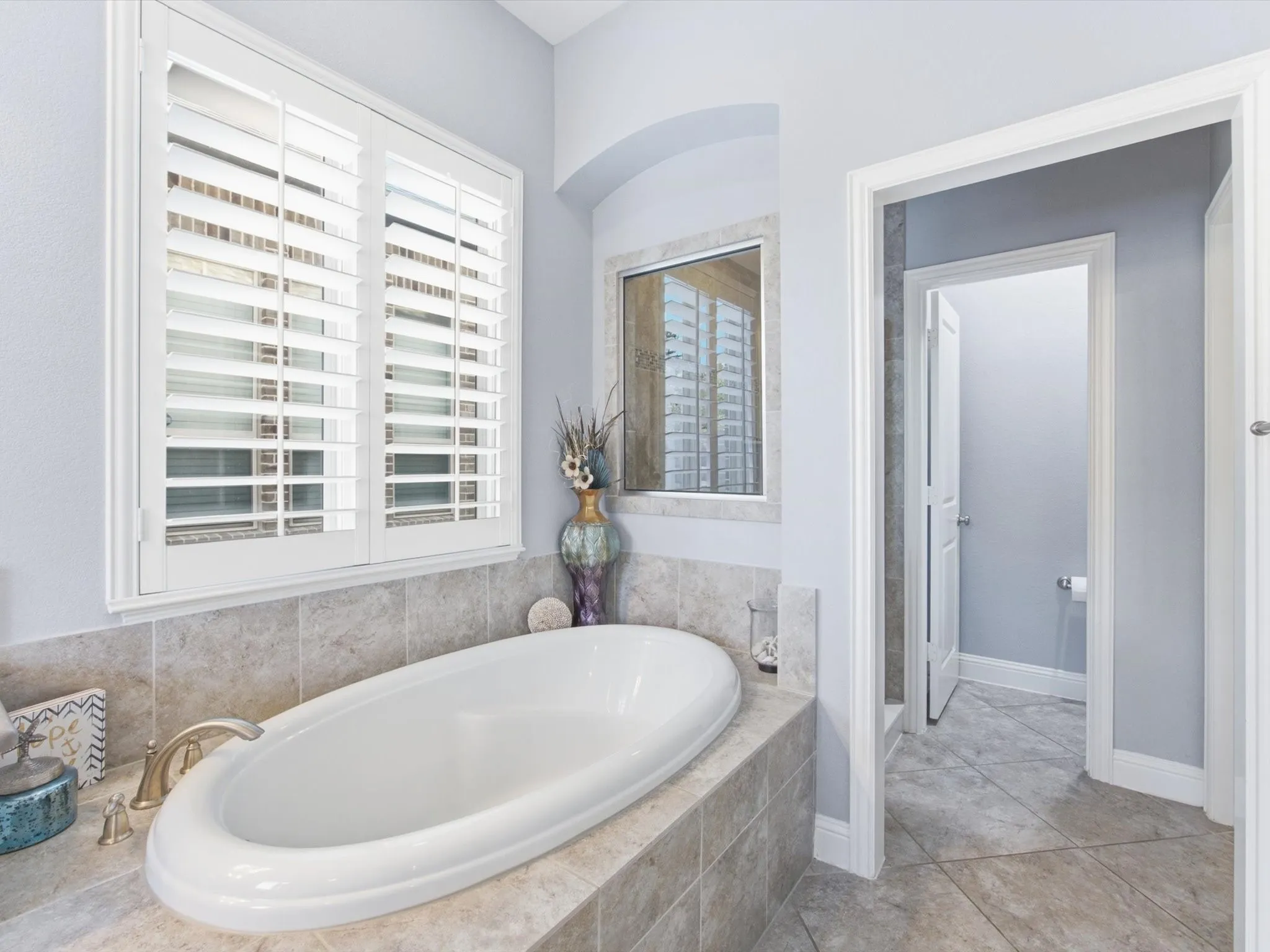 Oval soaking tub with deck-mounted brass-finish fixtures, surrounded by large format tile