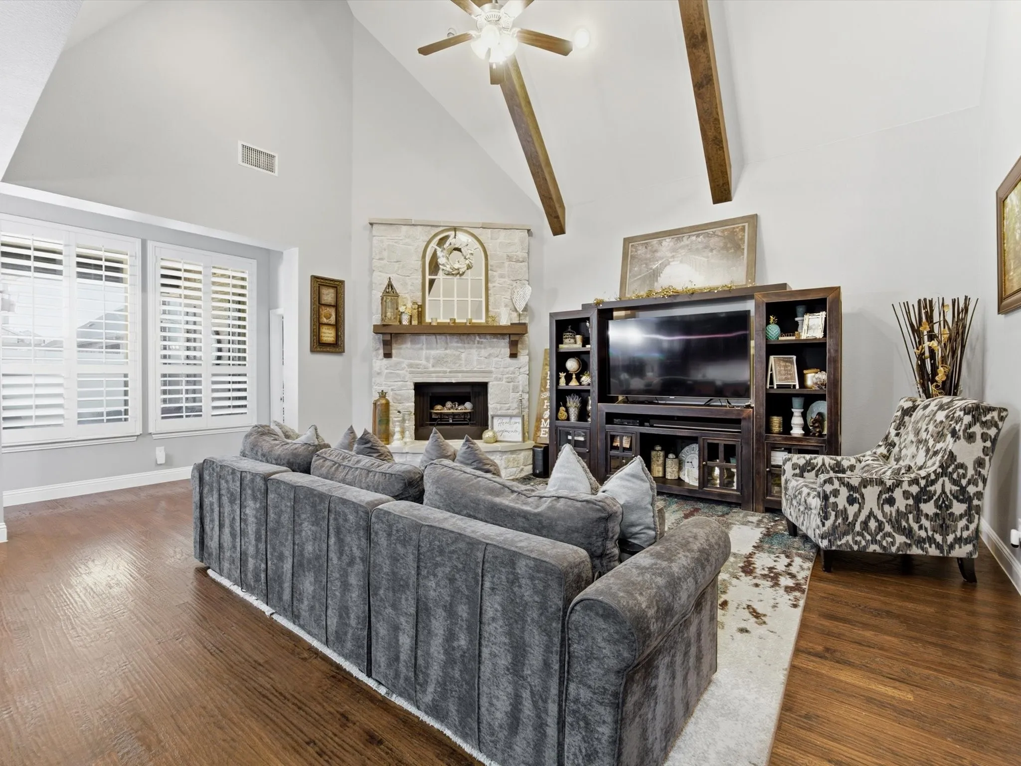 Spacious living area featuring a vaulted ceiling with exposed wood beams, a stone-clad fireplace, and wood-finish​​‌​​​​‌​​‌‌​‌‌​​​‌‌​‌​‌​‌​​​‌​​ flooring