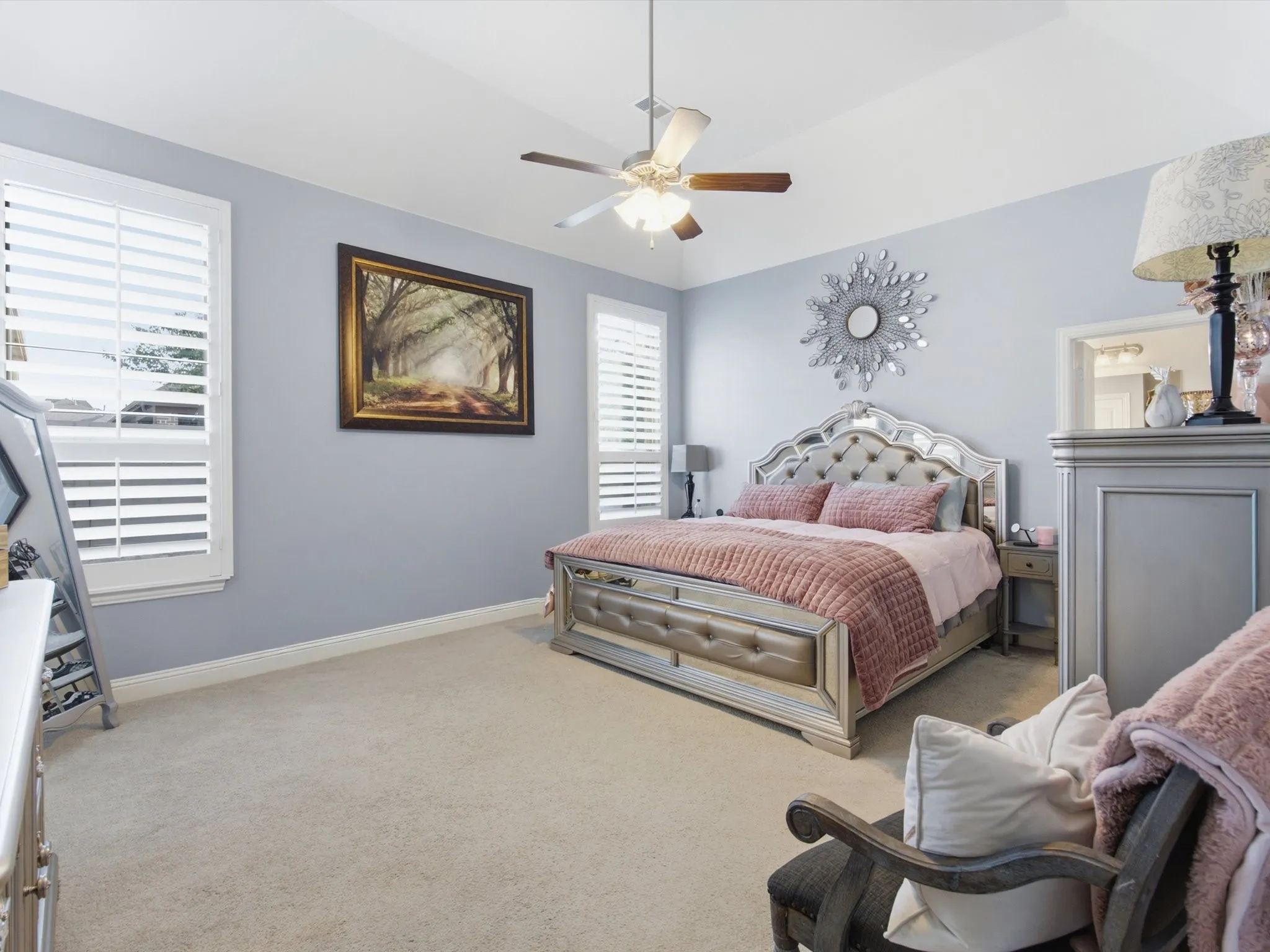 Spacious Primary Bedroom featuring vaulted ceilings, light-toned carpeting, two windows with white plantation shutters, and a ceiling fan with integrated lighting