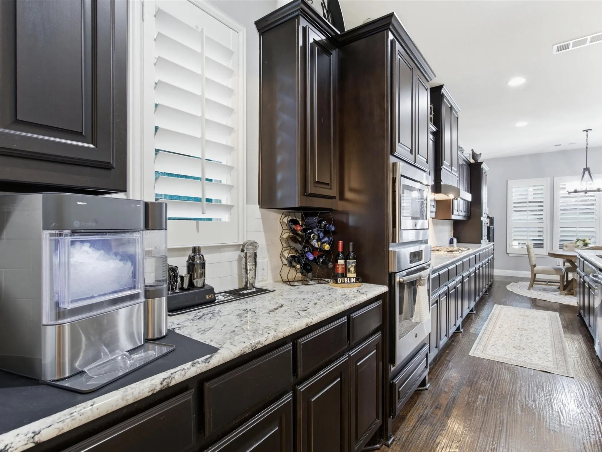 Kitchen featuring extensive dark cabinetry, light granite countertops, stainless steel appliances, and wood-finish flooring