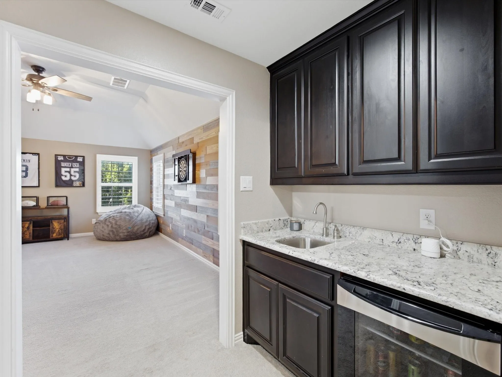 Integrated wet bar featuring dark cabinetry, a speckled countertop, a stainless steel sink, and a built-in beverage refrigerator