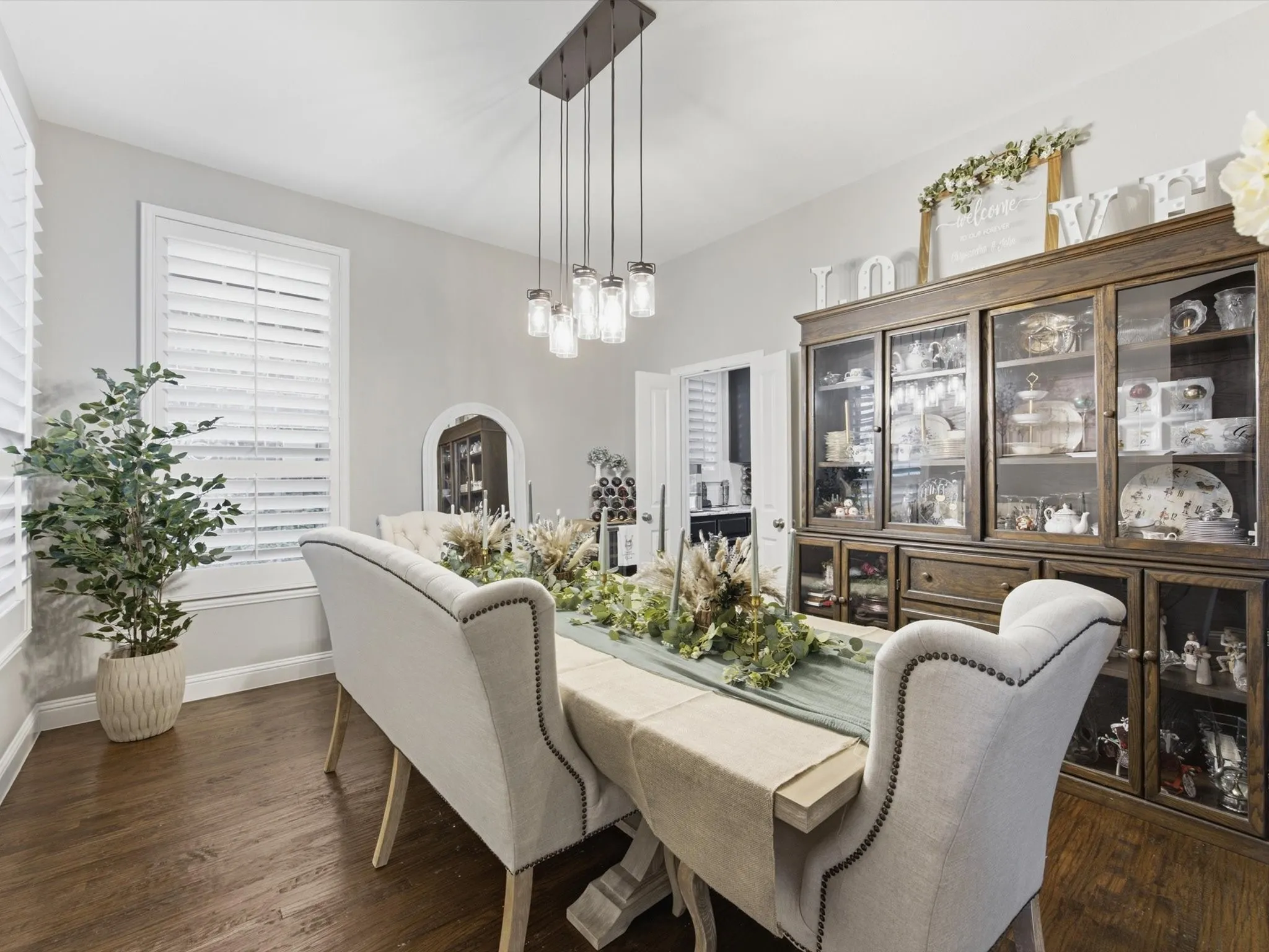 Dining area with wood-finish flooring, white plantation shutters, and a linear pendant light fixture