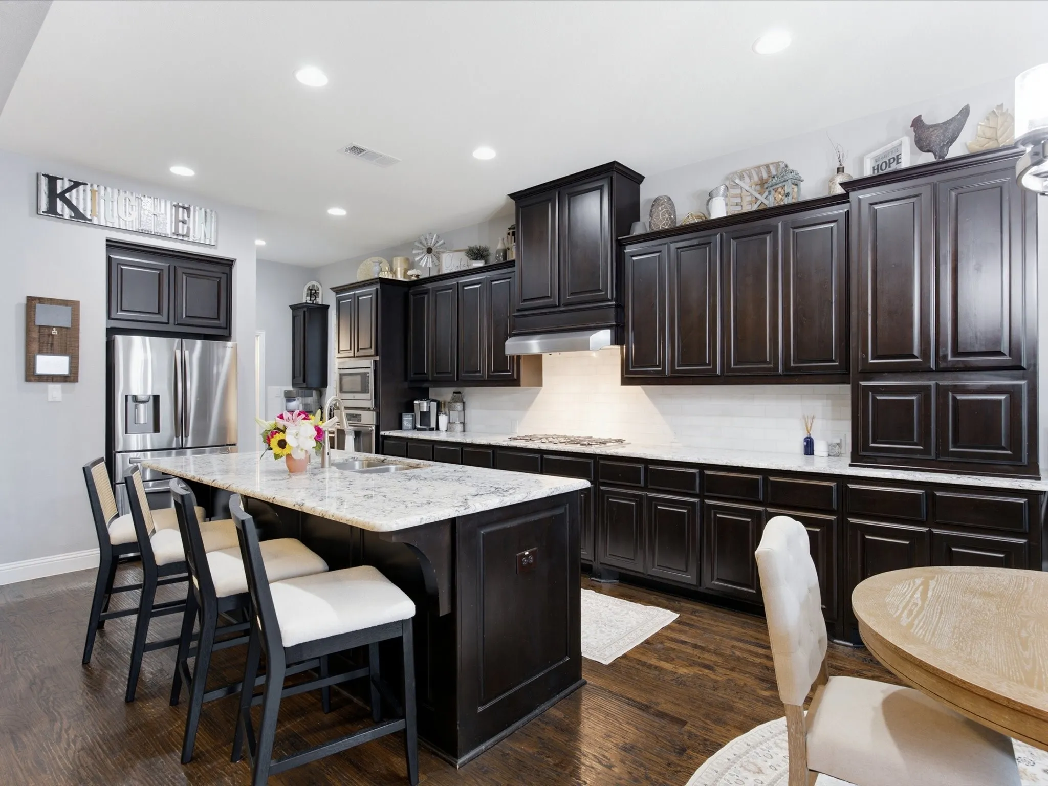 Kitchen featuring dark wood cabinetry, a central island with a light-colored countertop, stainless steel refrigerator, built-in microwave, and wood-finish flooring
