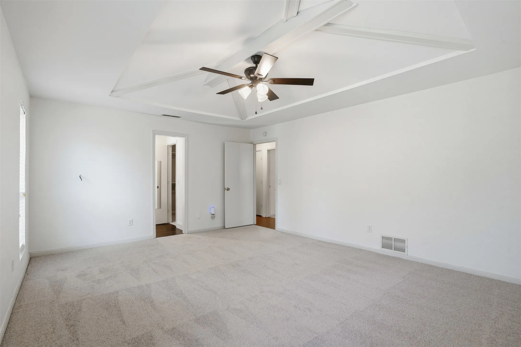 Spacious room featuring a decorative tray ceiling with exposed white beams and a ceiling fan