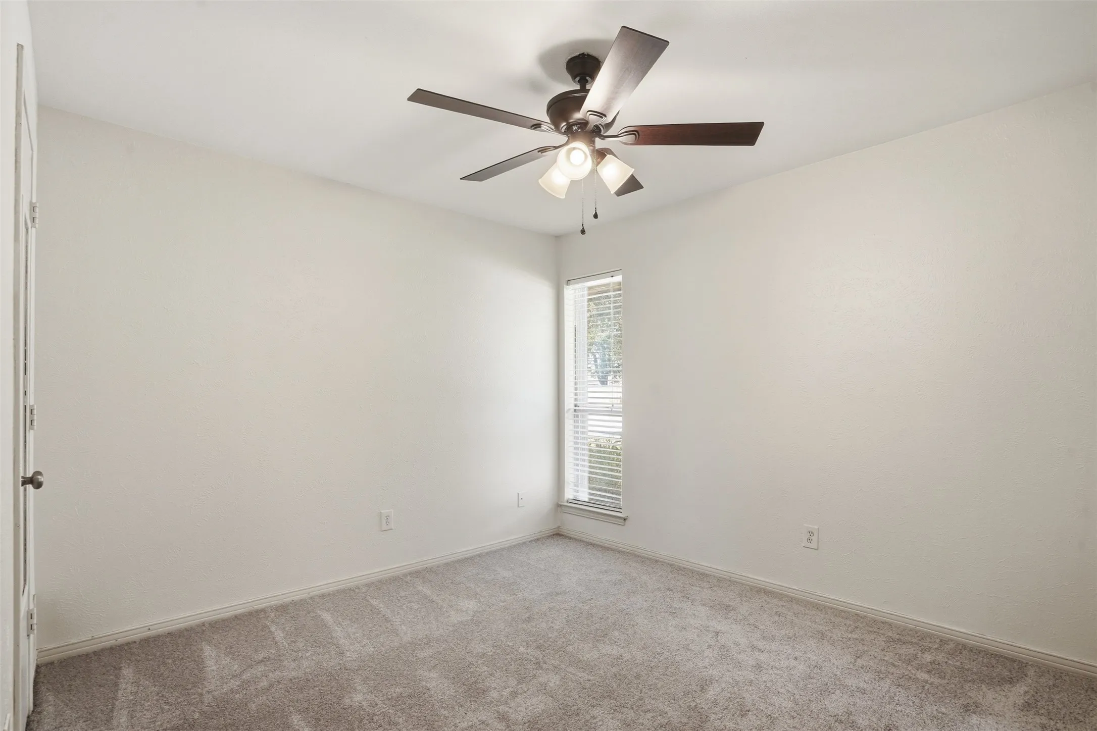 Carpeted room with a ceiling fan light fixture, light-colored walls, and a window with blinds