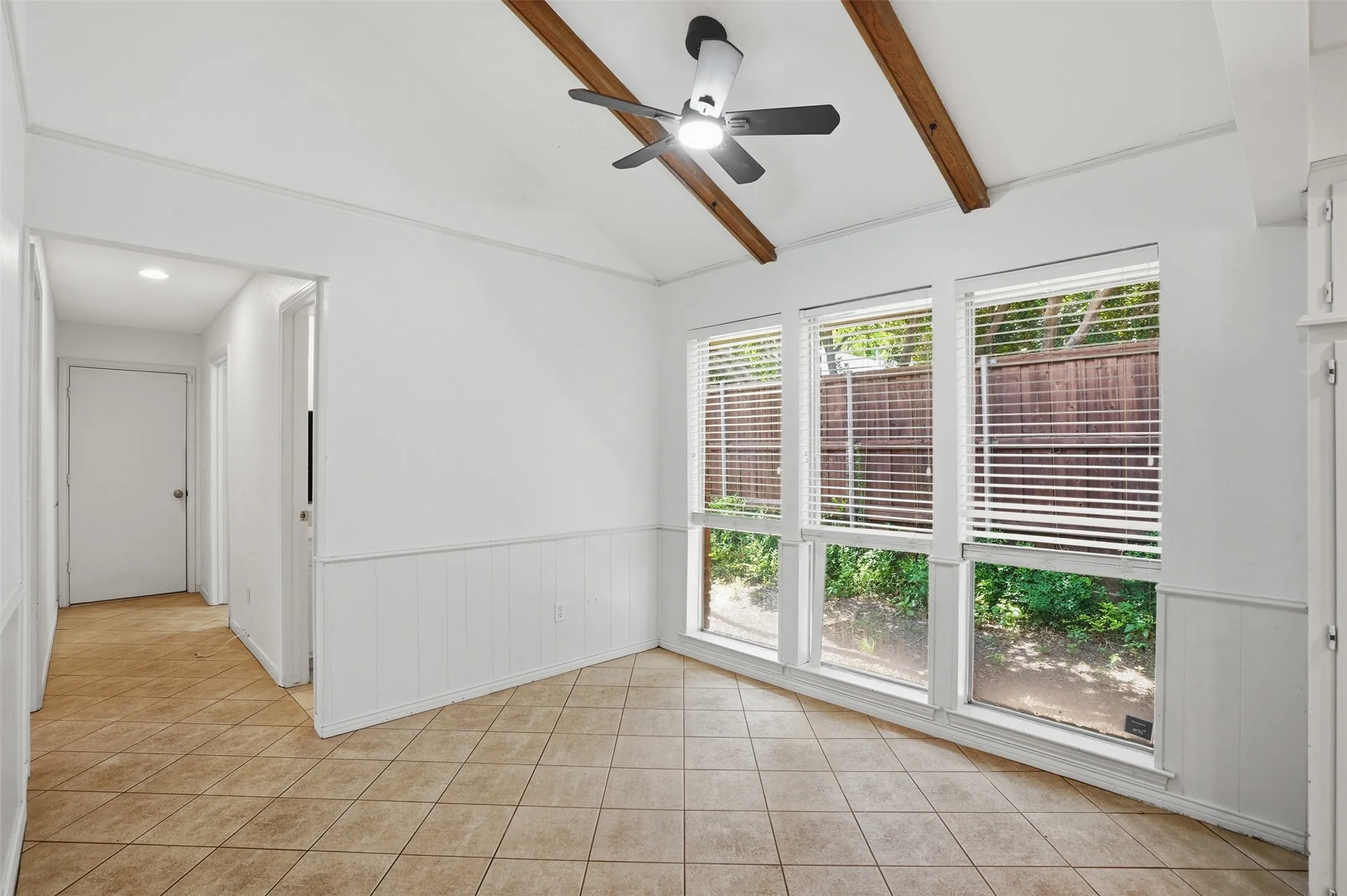 Room featuring a vaulted ceiling with exposed wood beams, a modern ceiling fan, and large windows with blinds