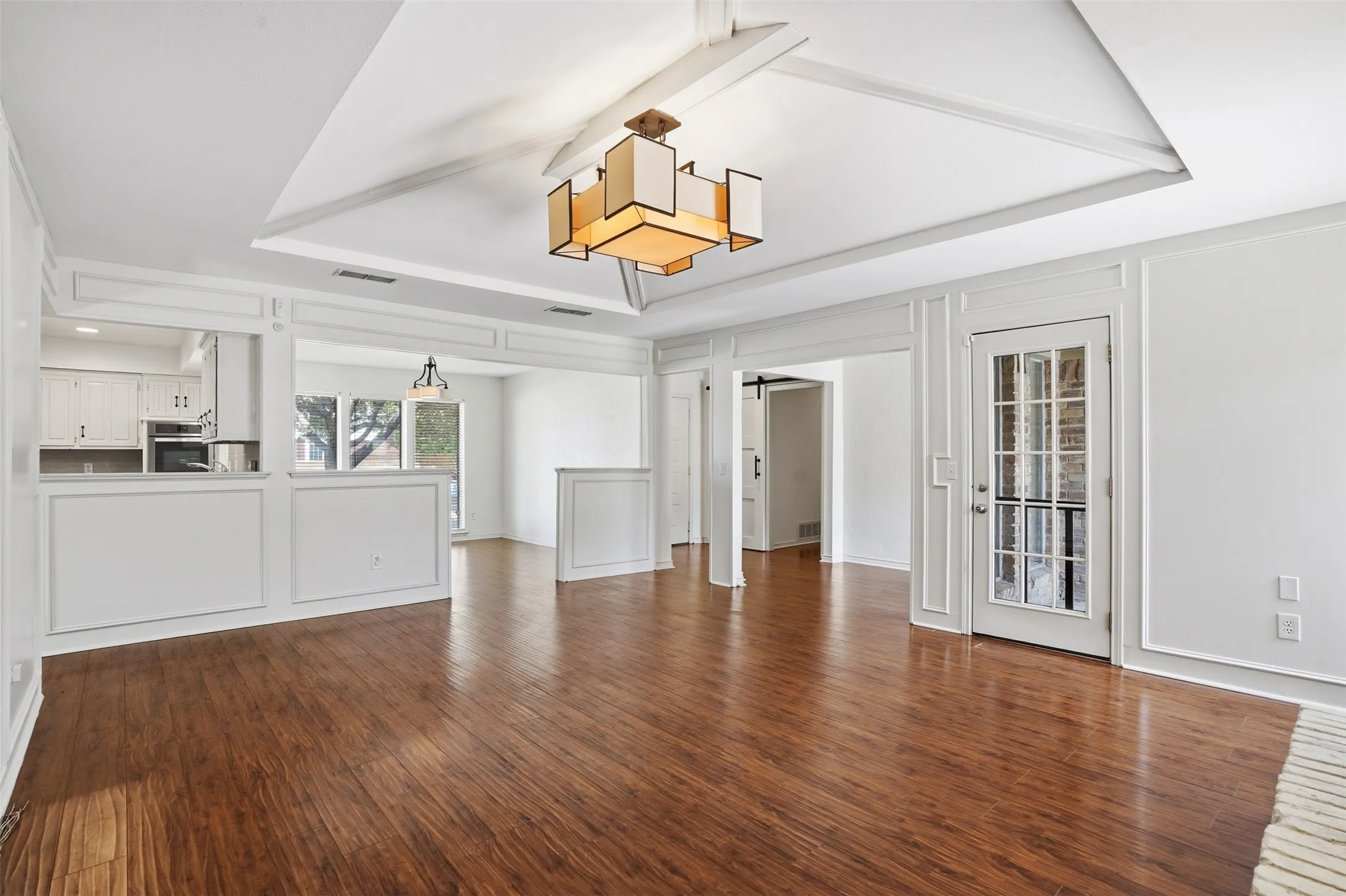 Open concept living area featuring wood-finish flooring, a tray ceiling with exposed beams, and a modern rectangular chandelier