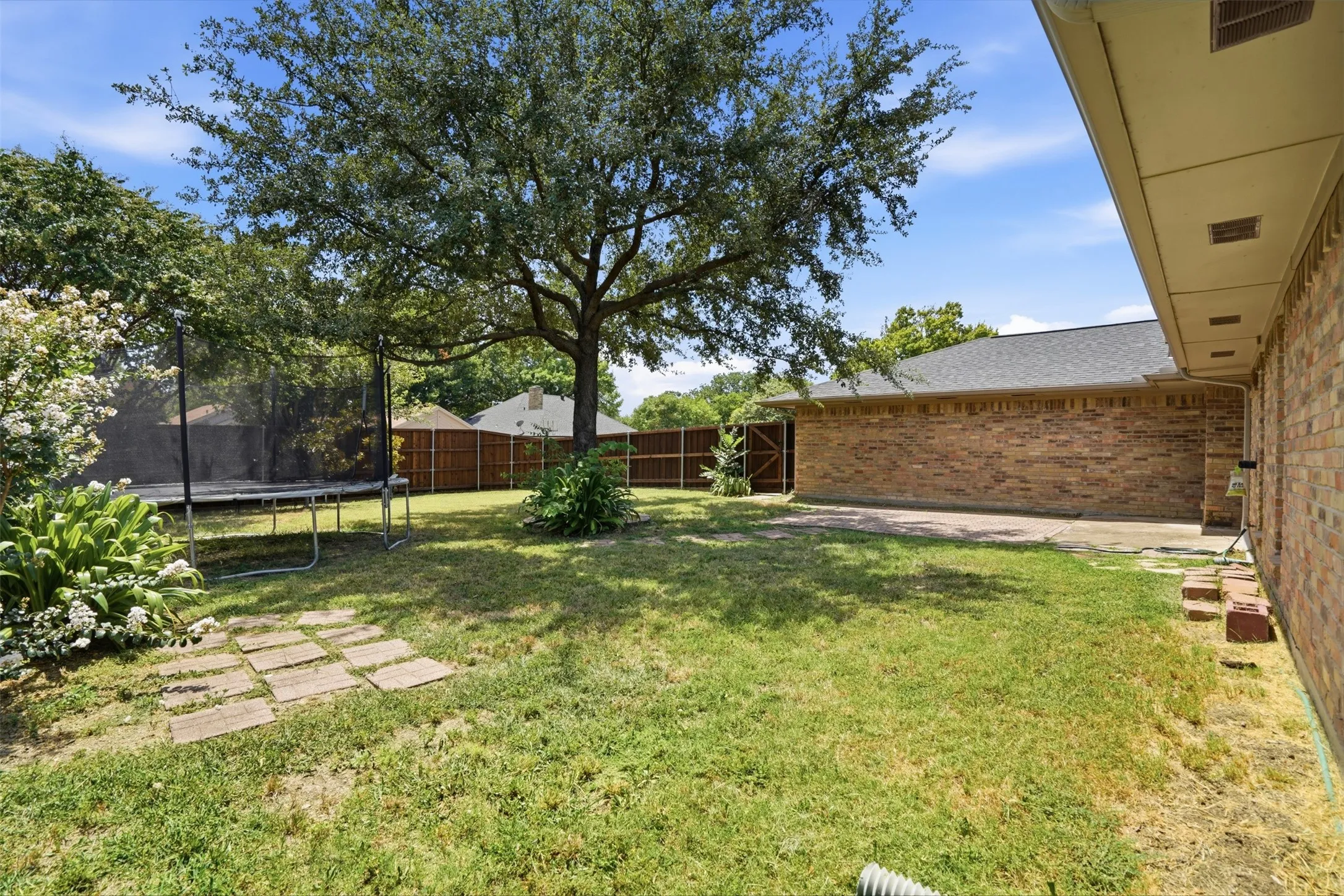 Expansive rear yard featuring a large mature tree, a paved patio area, and a brick exterior wall