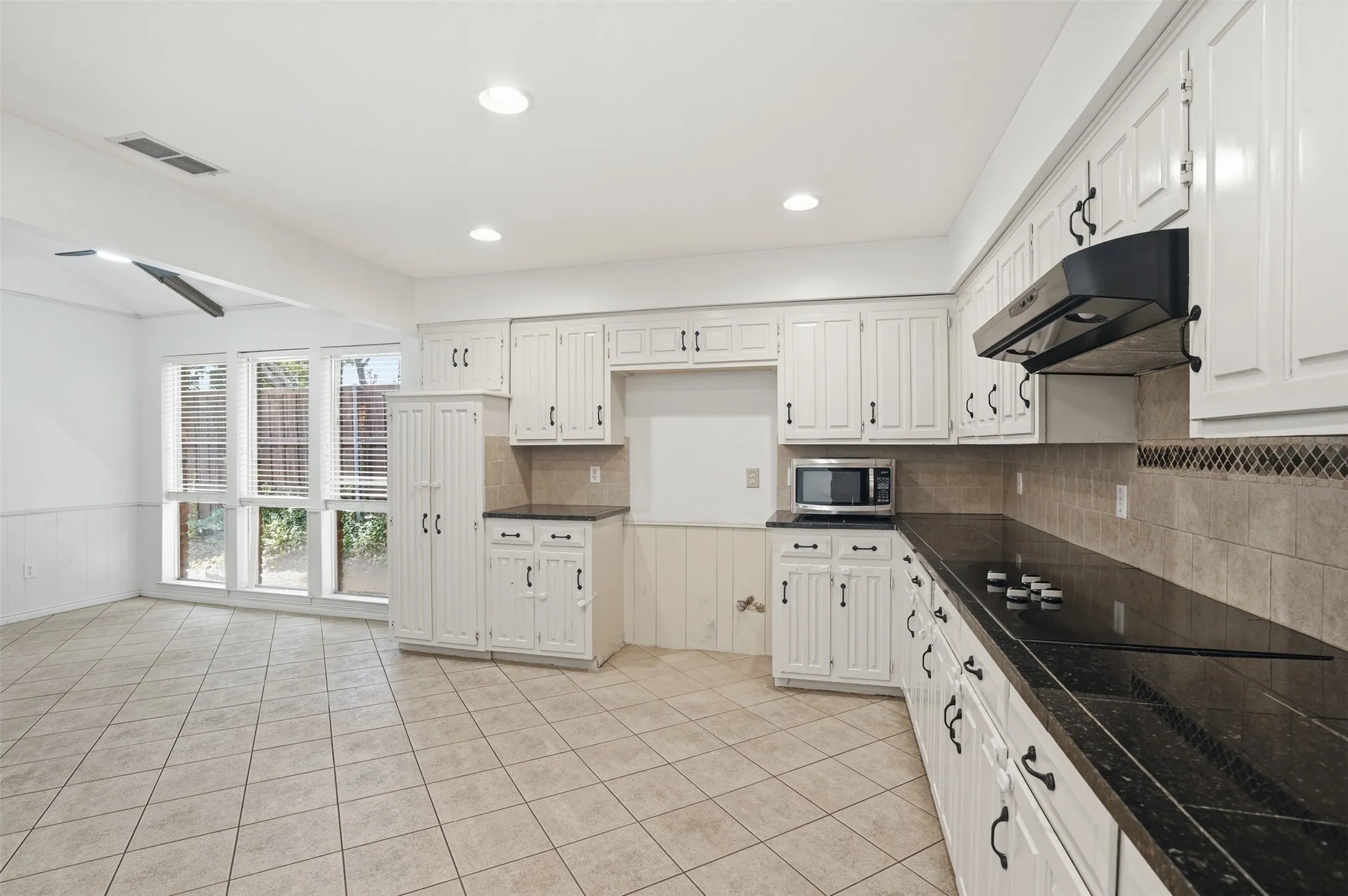 Kitchen featuring white cabinetry, black stone countertops, and a tiled backsplash