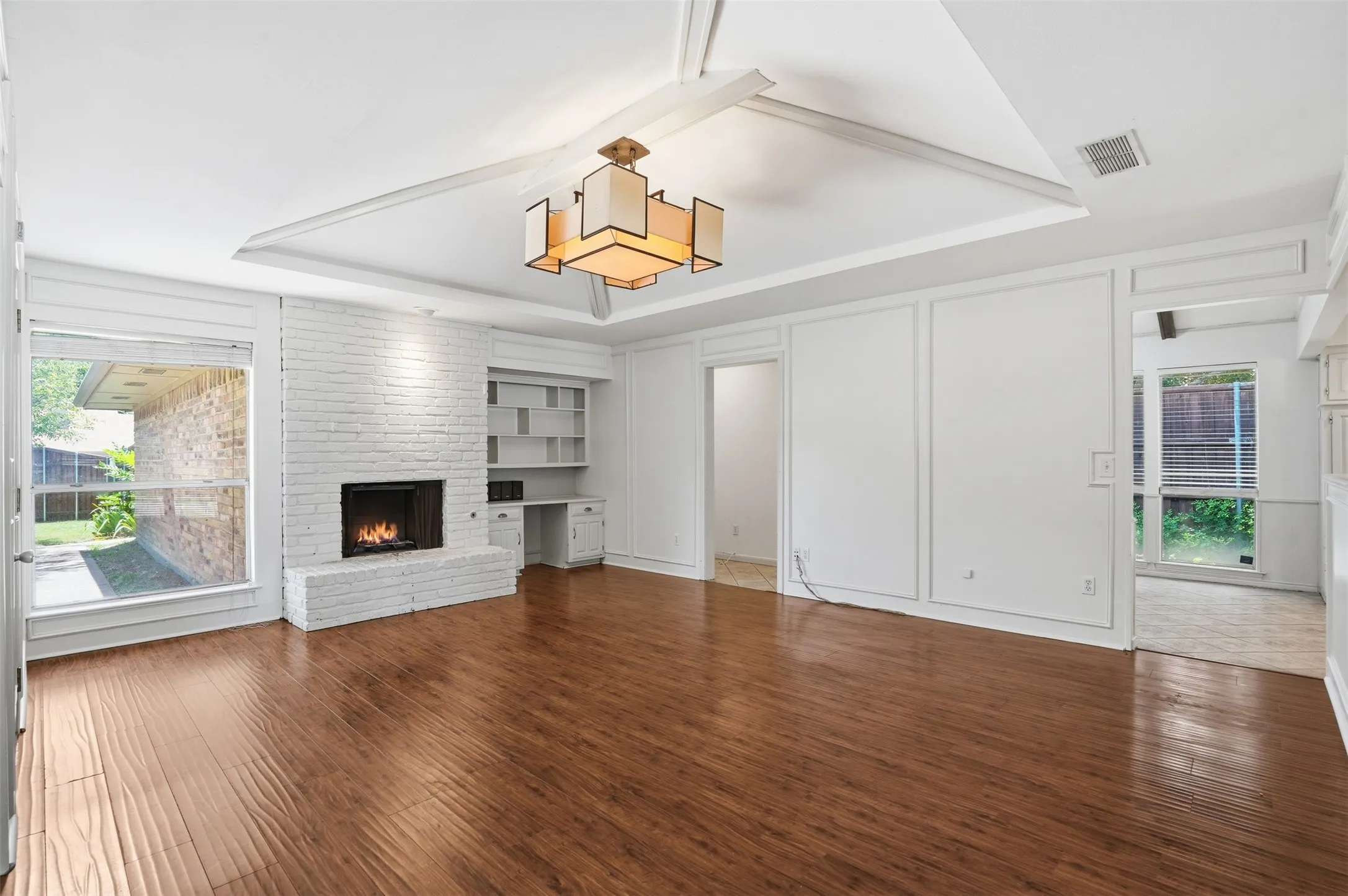 Spacious living area featuring wood-finish flooring, a white brick fireplace, and extensive built-in shelving