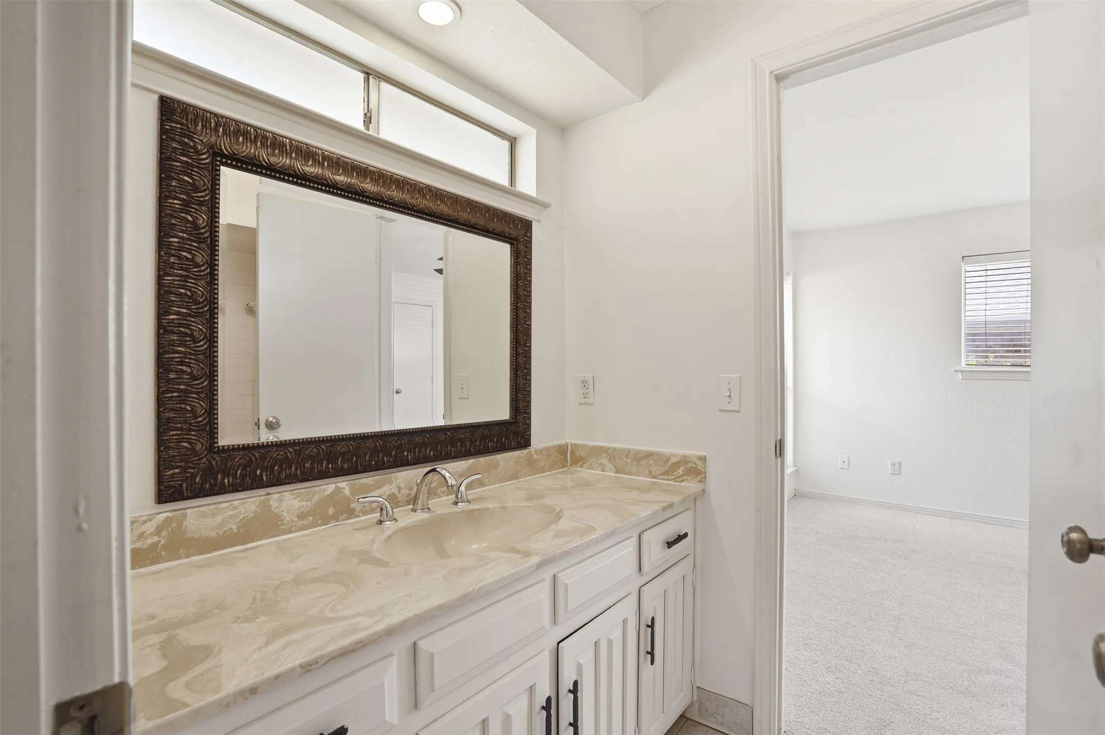 Bathroom vanity featuring a single integrated sink, stone-finish countertop, and white cabinetry with dark hardware