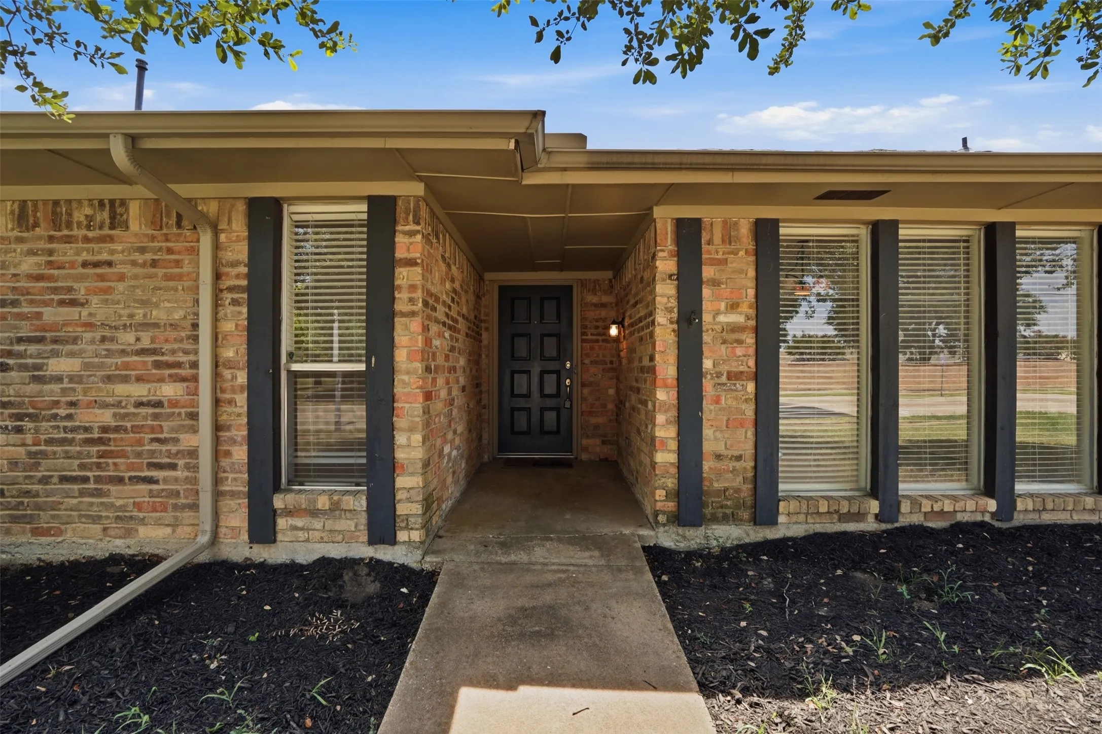 Brick facade residence featuring a covered entry, dark paneled front door, and multiple front-facing windows with blinds